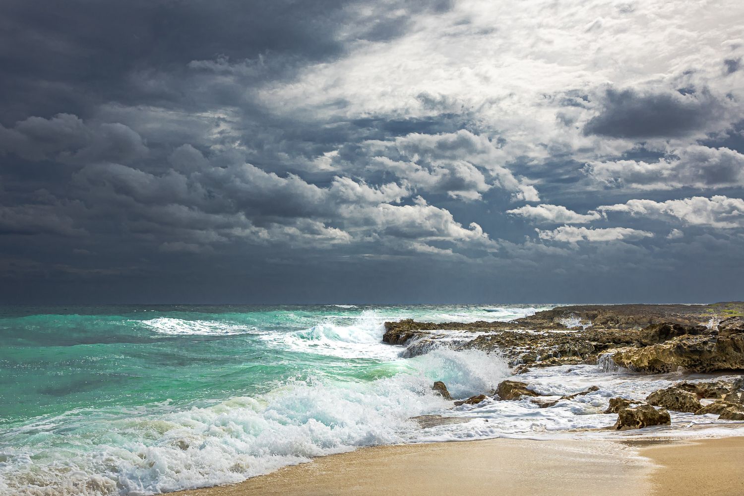 Waves crashing against rocky coastline in Cozumel, Mexico under dramatic storm clouds and turquoise Caribbean water.