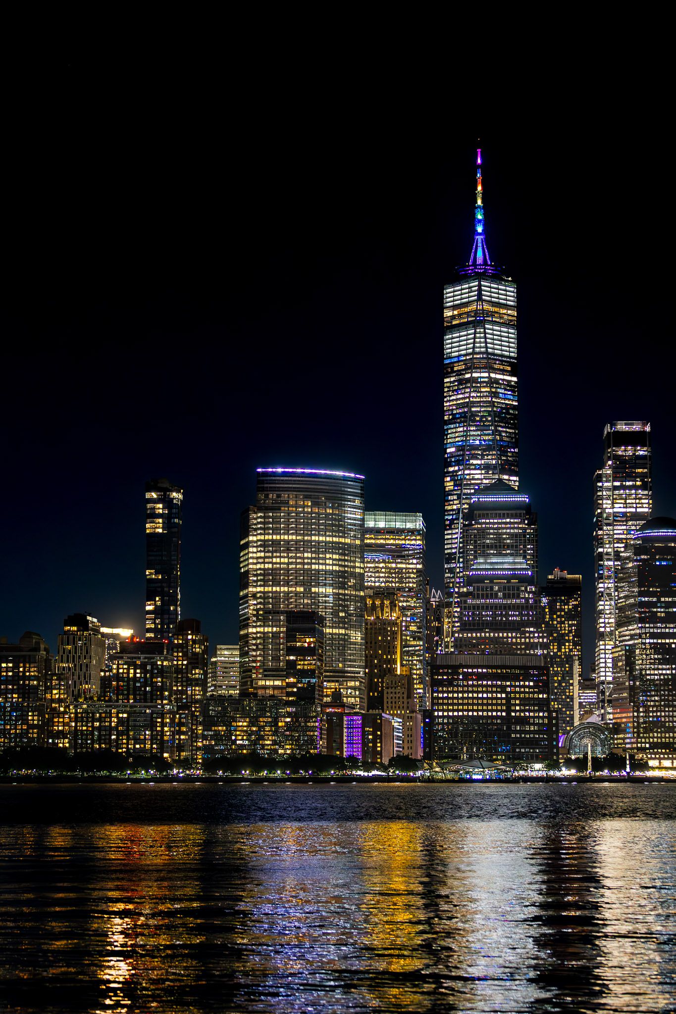 New York City skyline at night with One World Trade Center illuminated, viewed across the Hudson River from Jersey City, New Jersey.