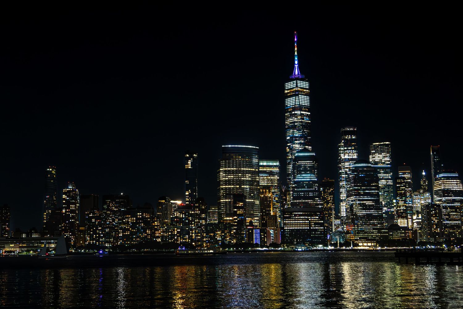 New York City skyline at night with One World Trade Center illuminated, viewed across the Hudson River from Jersey City, New Jersey.