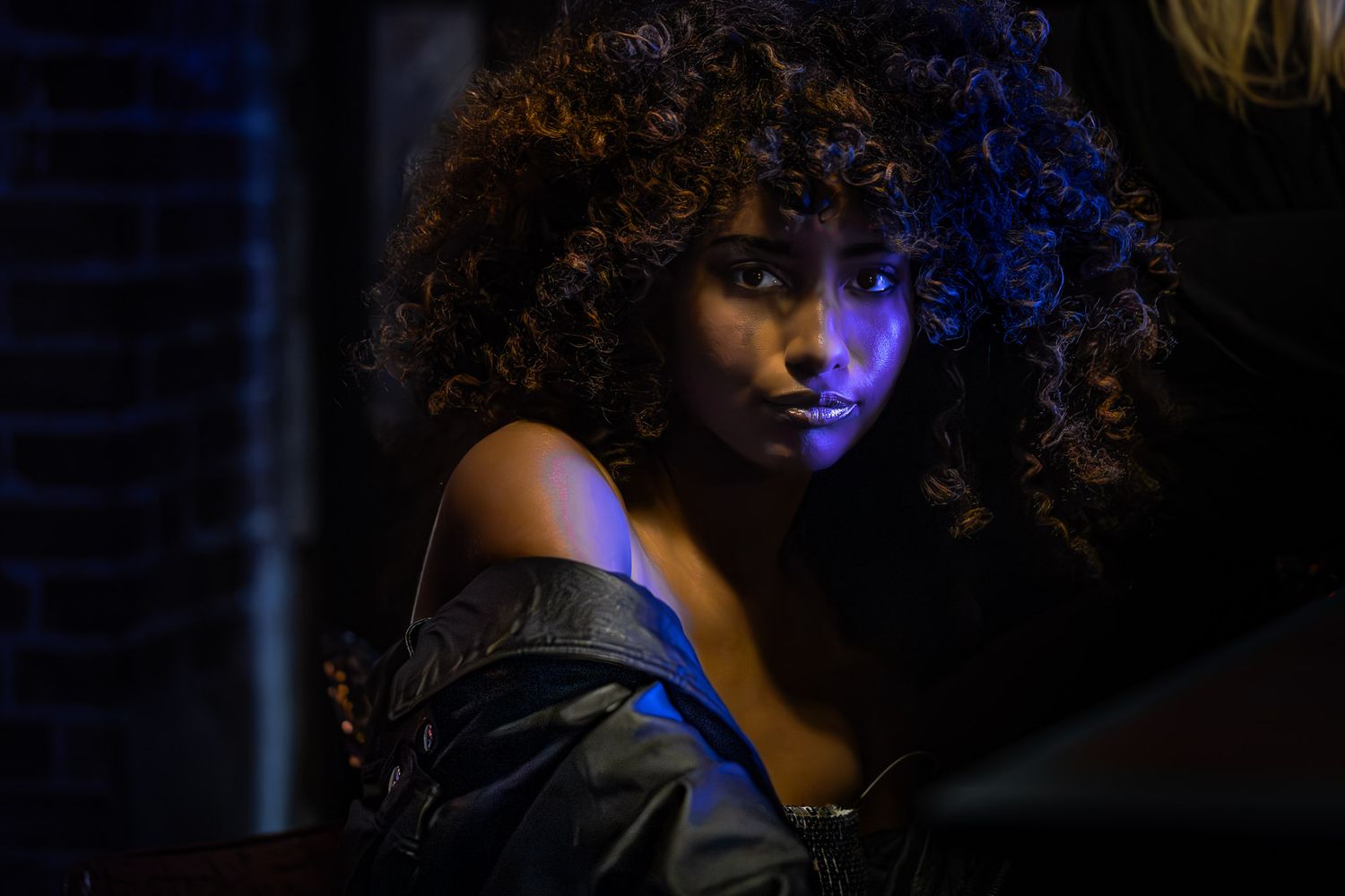 Moody studio portrait of woman with curly hair lit by dramatic blue and warm lighting during a Unique Photo photography event in PA