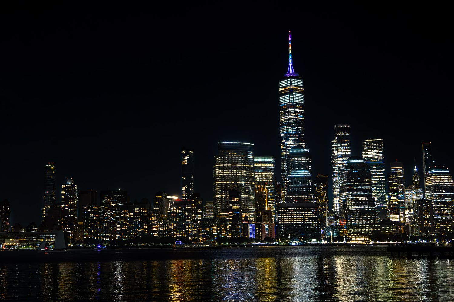 New York City skyline at night with One World Trade Center illuminated, viewed across the Hudson River from Jersey City, New Jersey.