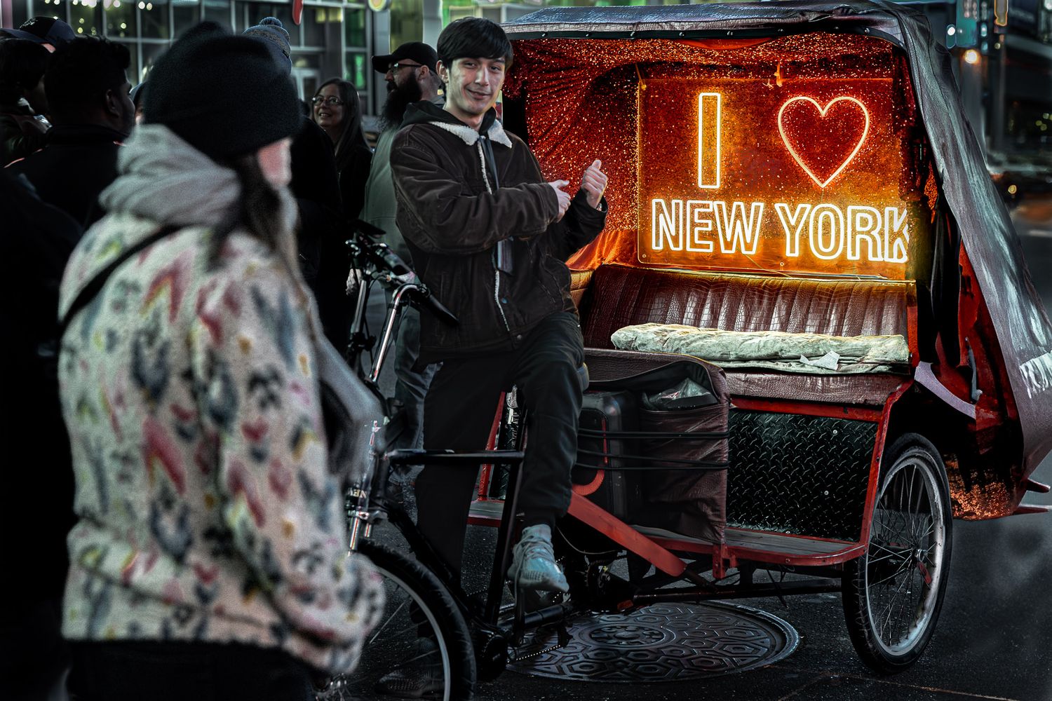 Pedicab driver posing beside an illuminated ‘I Love New York' sign during a candid street moment in Times Square at night.