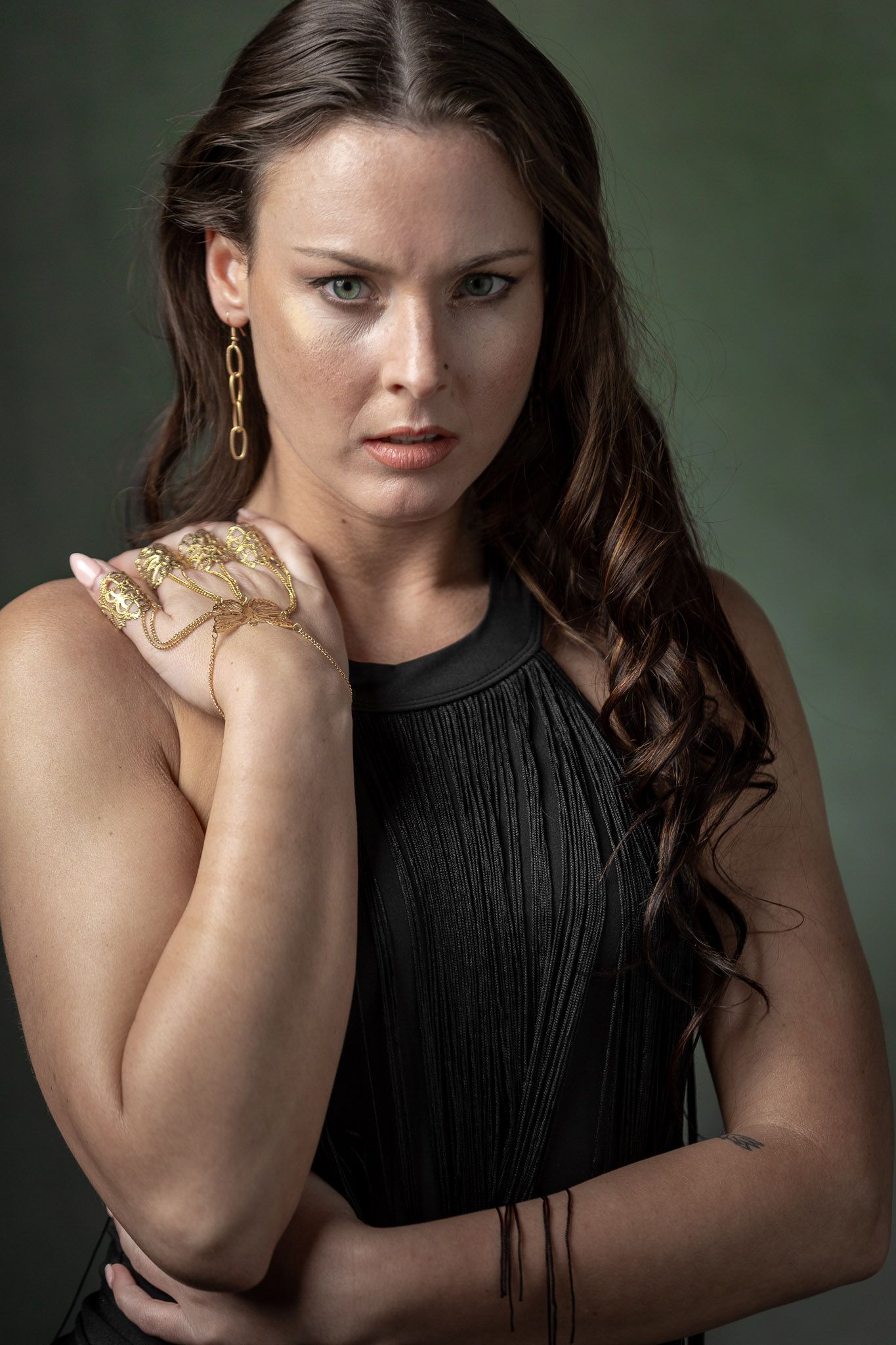 Studio portrait of a woman with green eyes wearing black attire and gold jewelry against a dark green background. during a Unique Photo phot