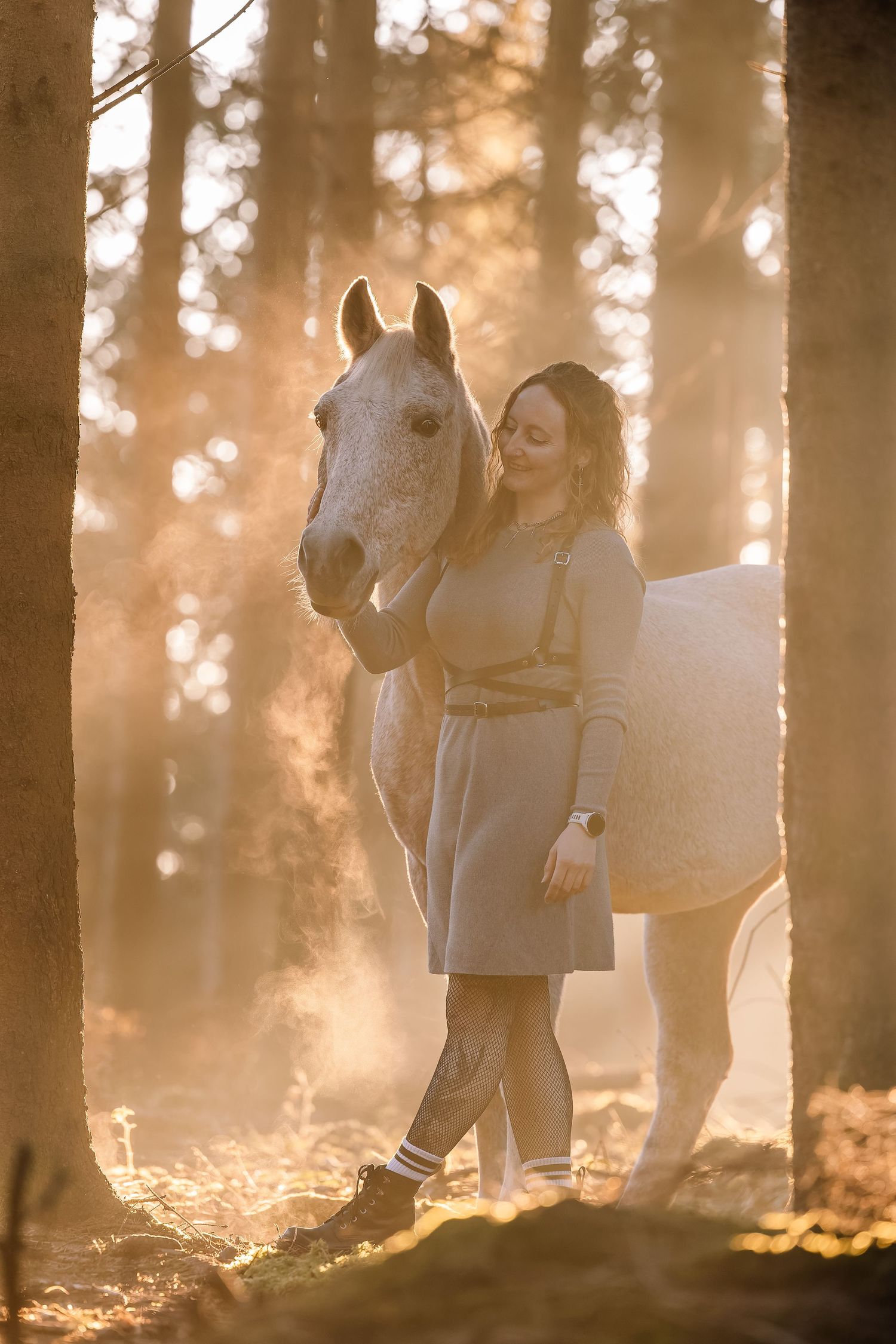Horses and their companions walk through a misty forest at sunset.