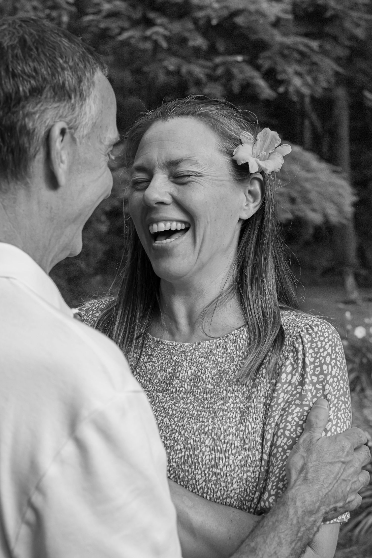 Black and white photo of woman with flower in hair laughing joyfully with man outdoors.