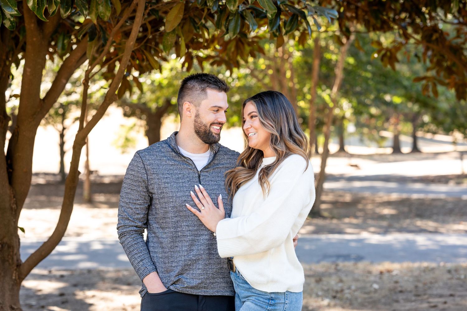 Romantic portrait of a couple embracing outdoors under sunlit trees.