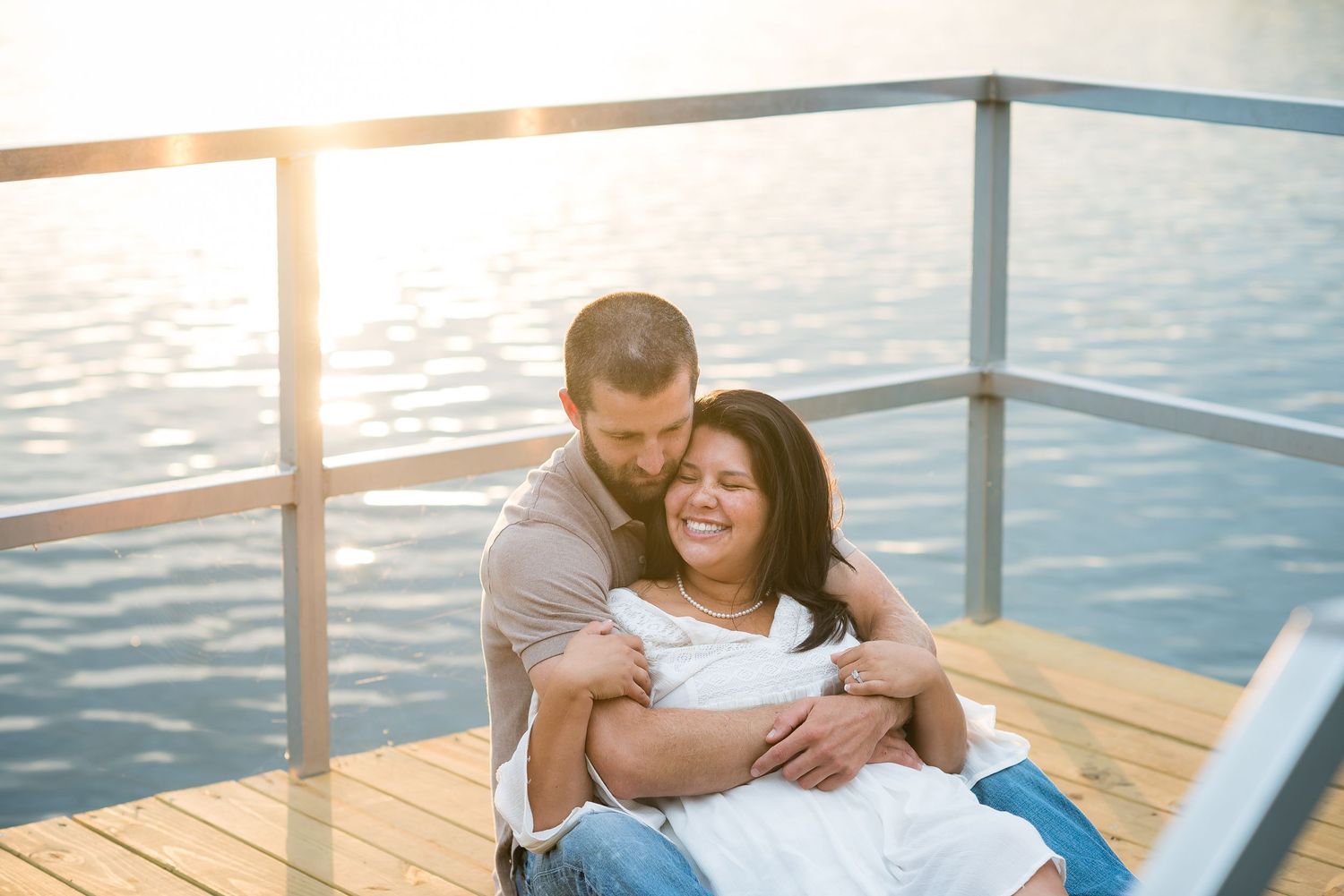 A tender moment shared on a dock at sunset with water reflections in the background.