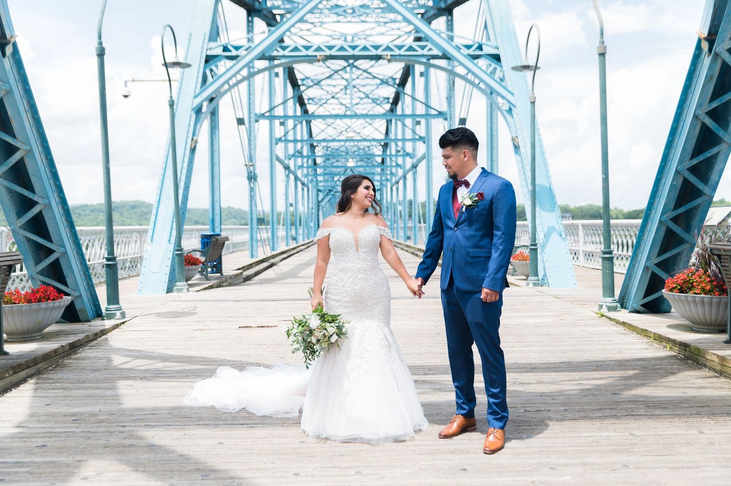 A wedding couple poses on a blue steel bridge in elegant attire.