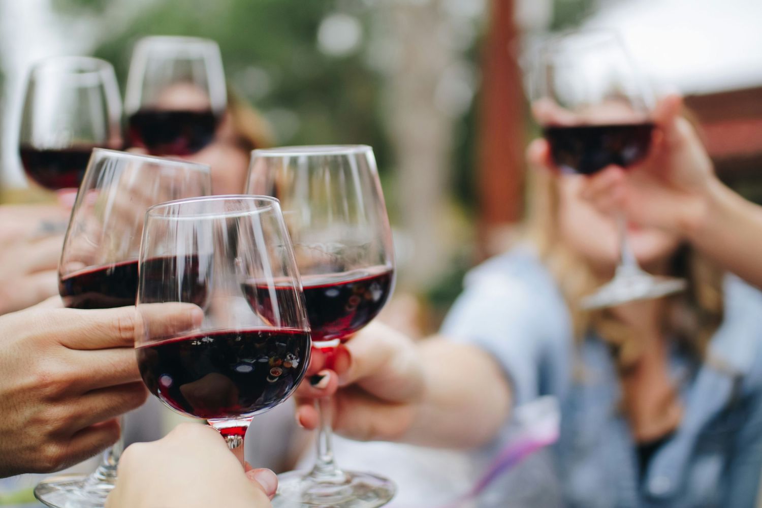 Friends toasting with glasses of red wine during an outdoor celebration.