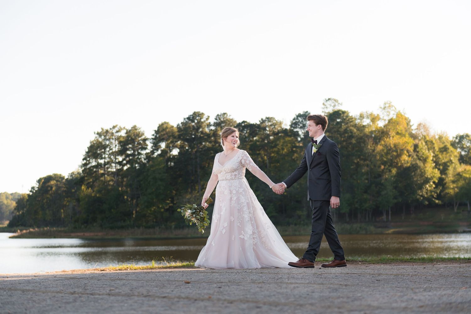 Wedding couple poses for romantic photos near lake at sunset.