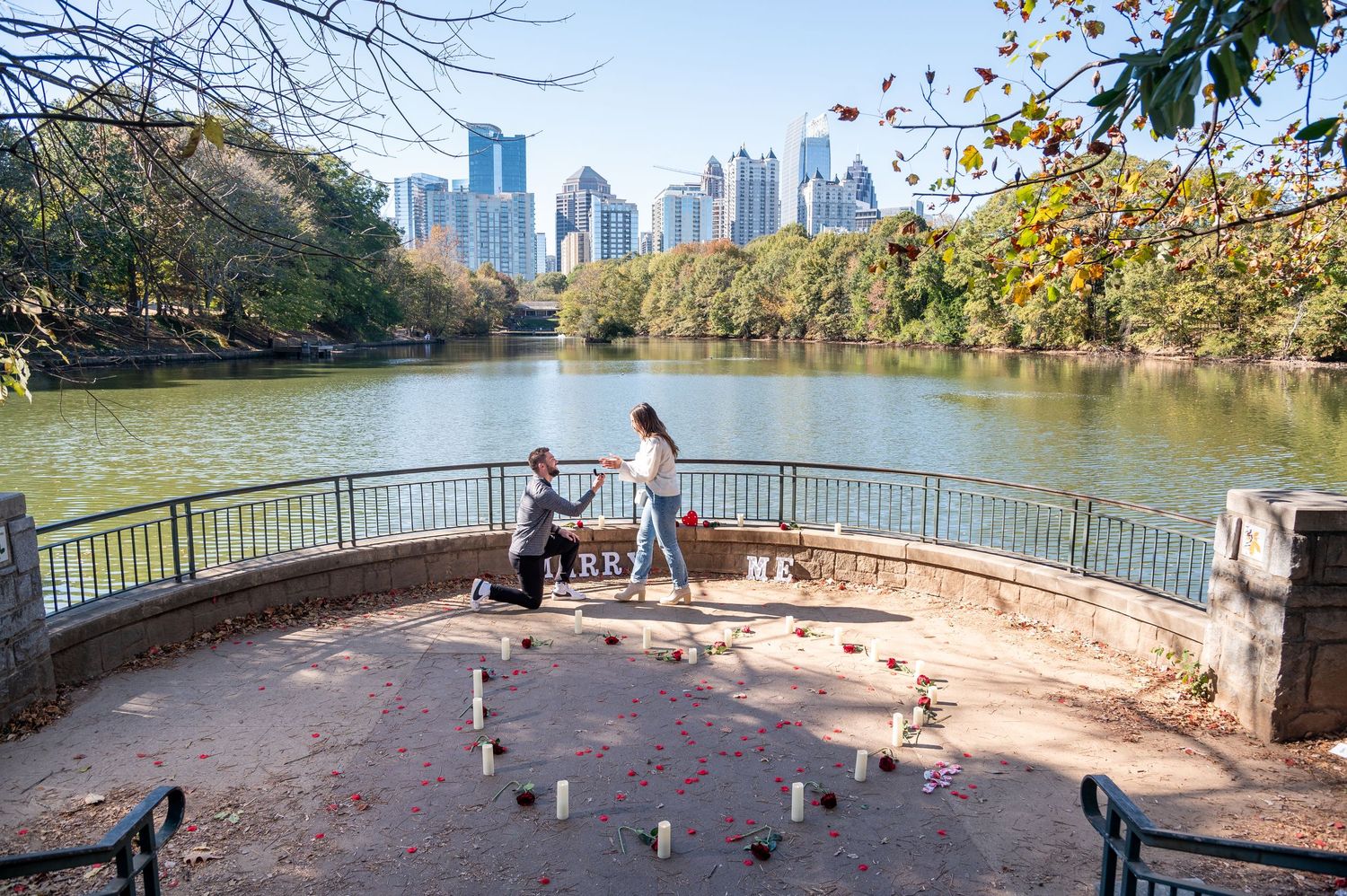 A romantic proposal setup with candles overlooking a city skyline and lake.