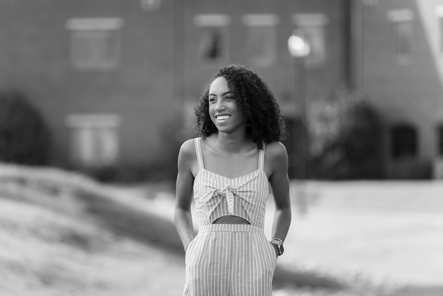 A woman in a striped sundress stands outdoors in a black and white portrait.