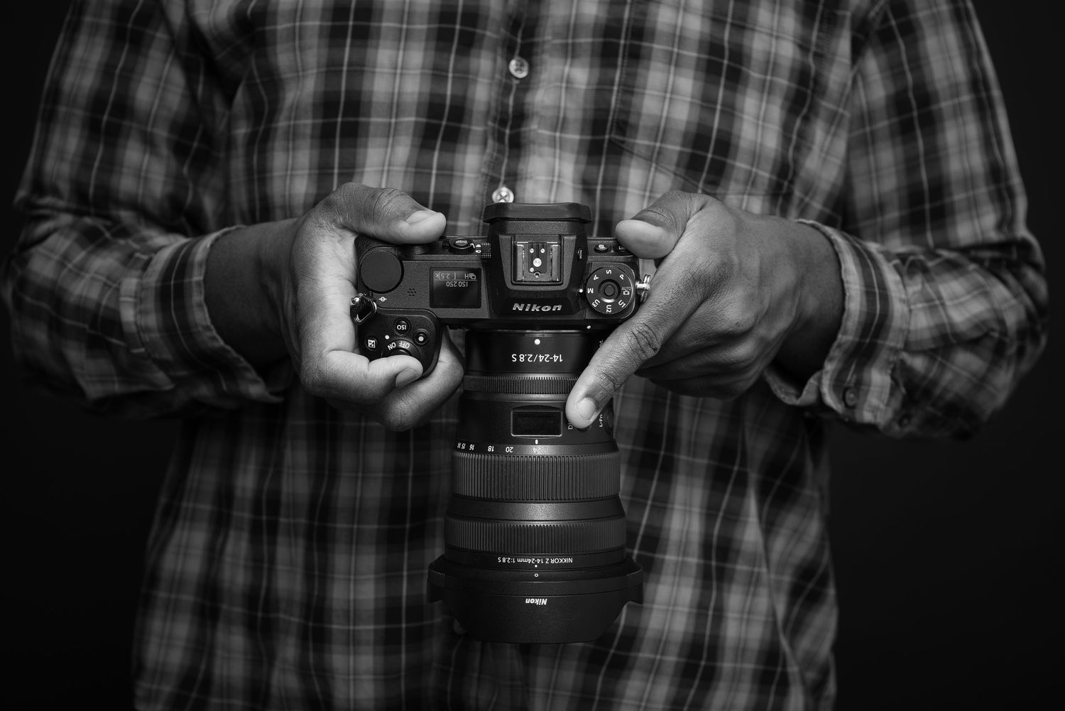 Close-up of hands holding DSLR camera showing top display screen in black and white.