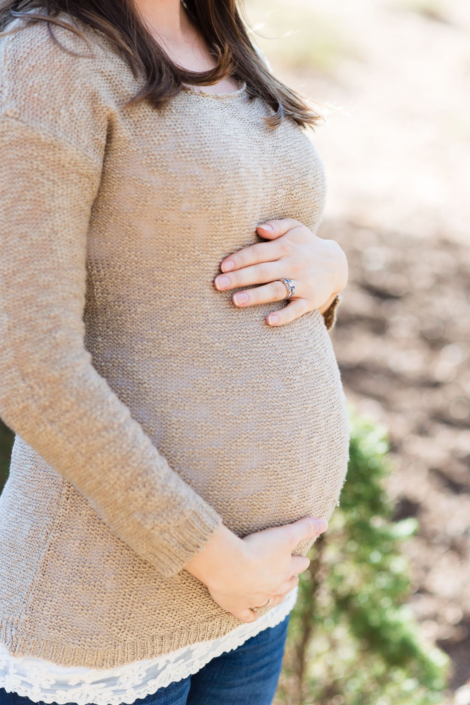 Close-up maternity photos showing gentle hands cradling a baby bump in soft sweater.