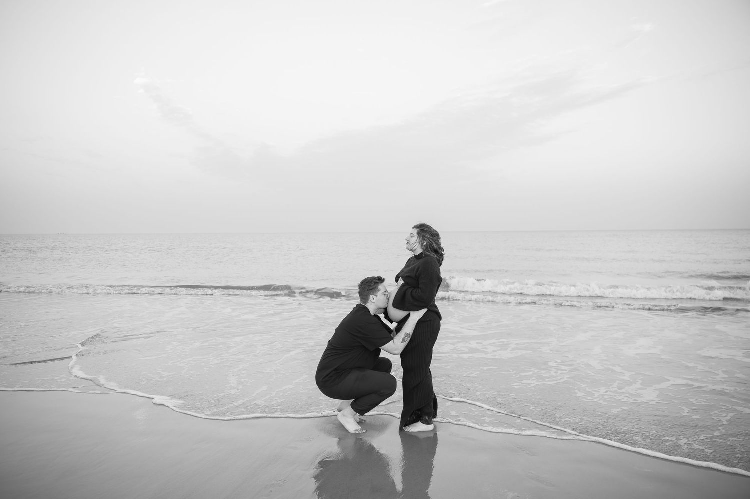 A black and white beach photo capturing a tender moment near the ocean waves.