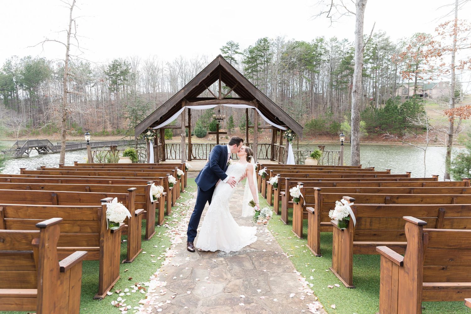 Outdoor wedding ceremony setup with wooden pews surrounded by trees and natural scenery.