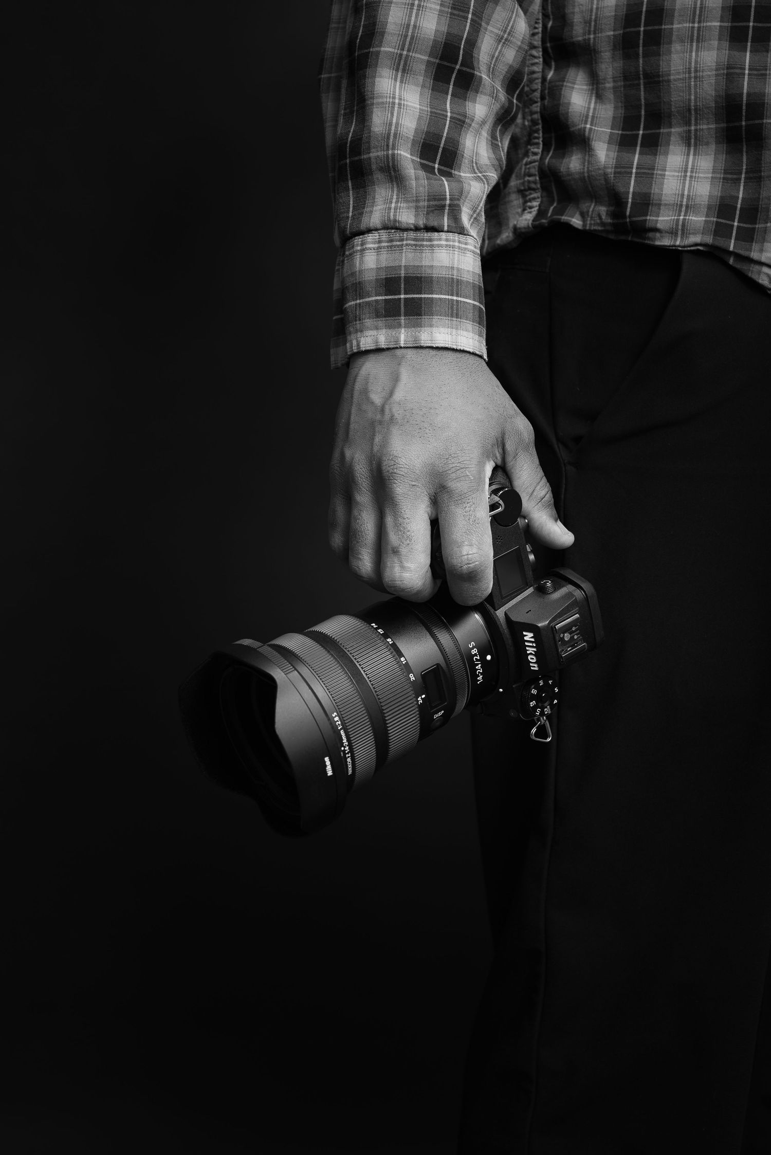 Black and white photo of hand holding professional camera with telephoto lens.