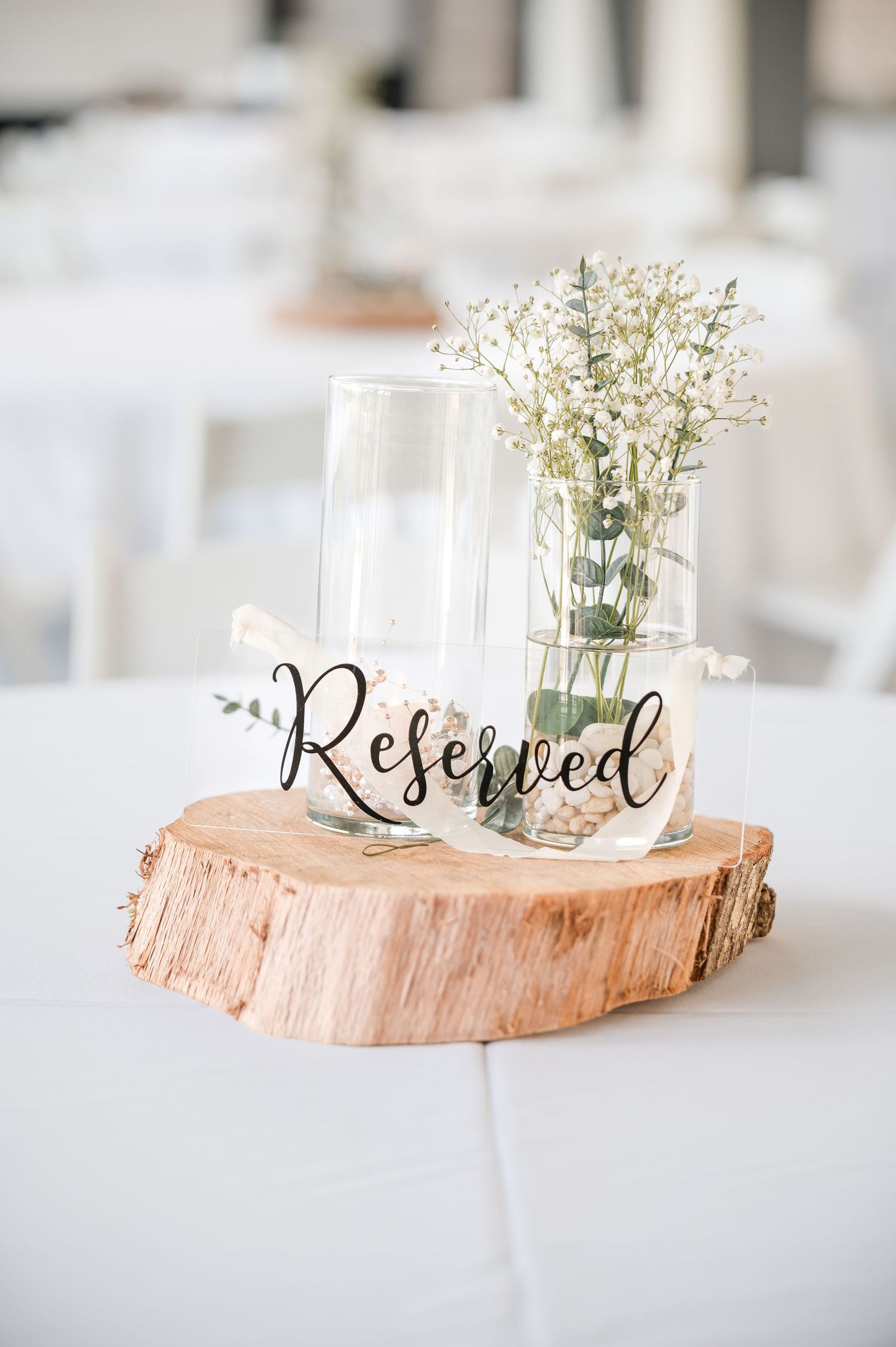 A rustic wedding table decoration featuring a Reserved sign on a wood slice with baby's breath in a glass vase.