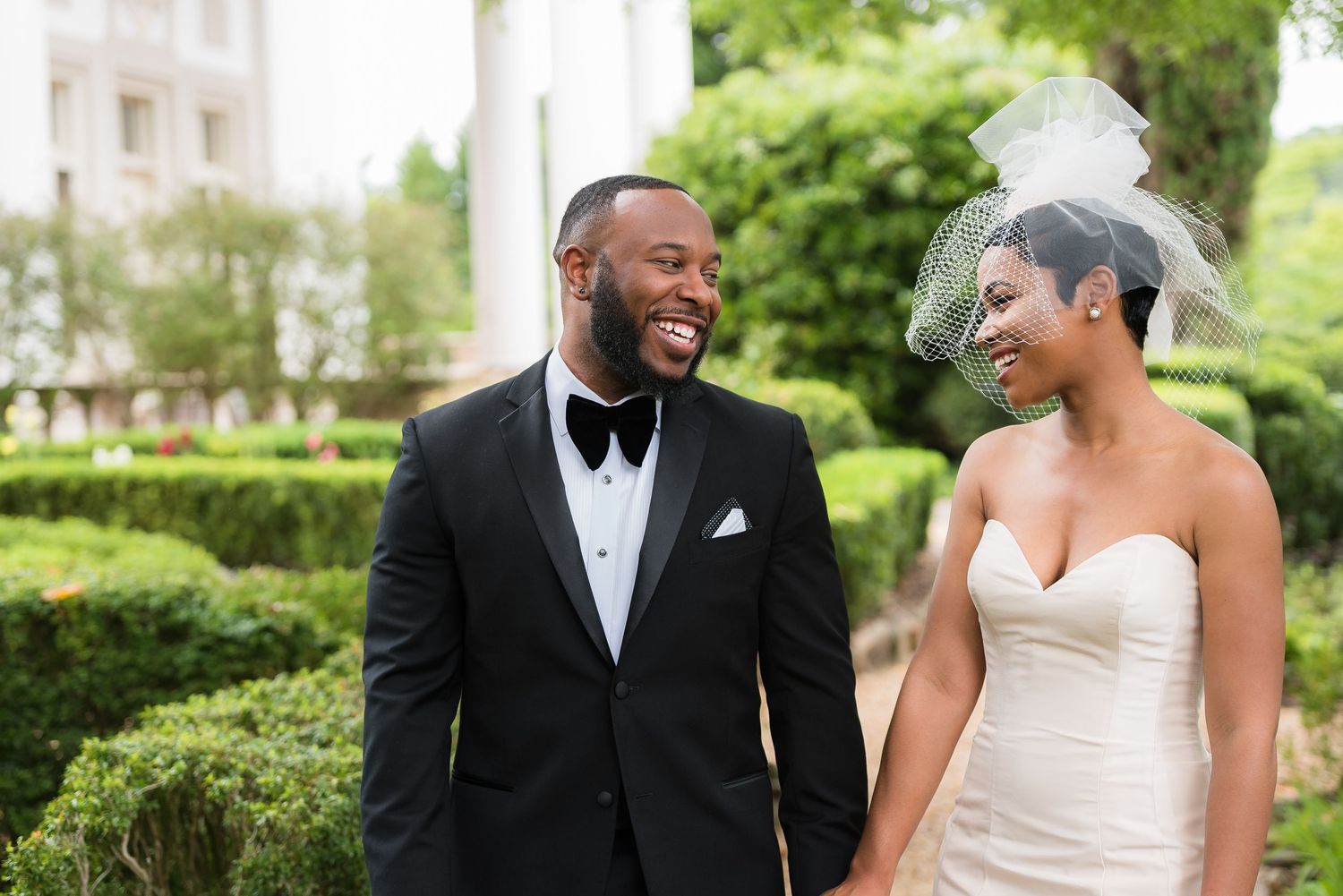 Outdoor garden wedding portraits in front of lush greenery with a blue suit and white dress.