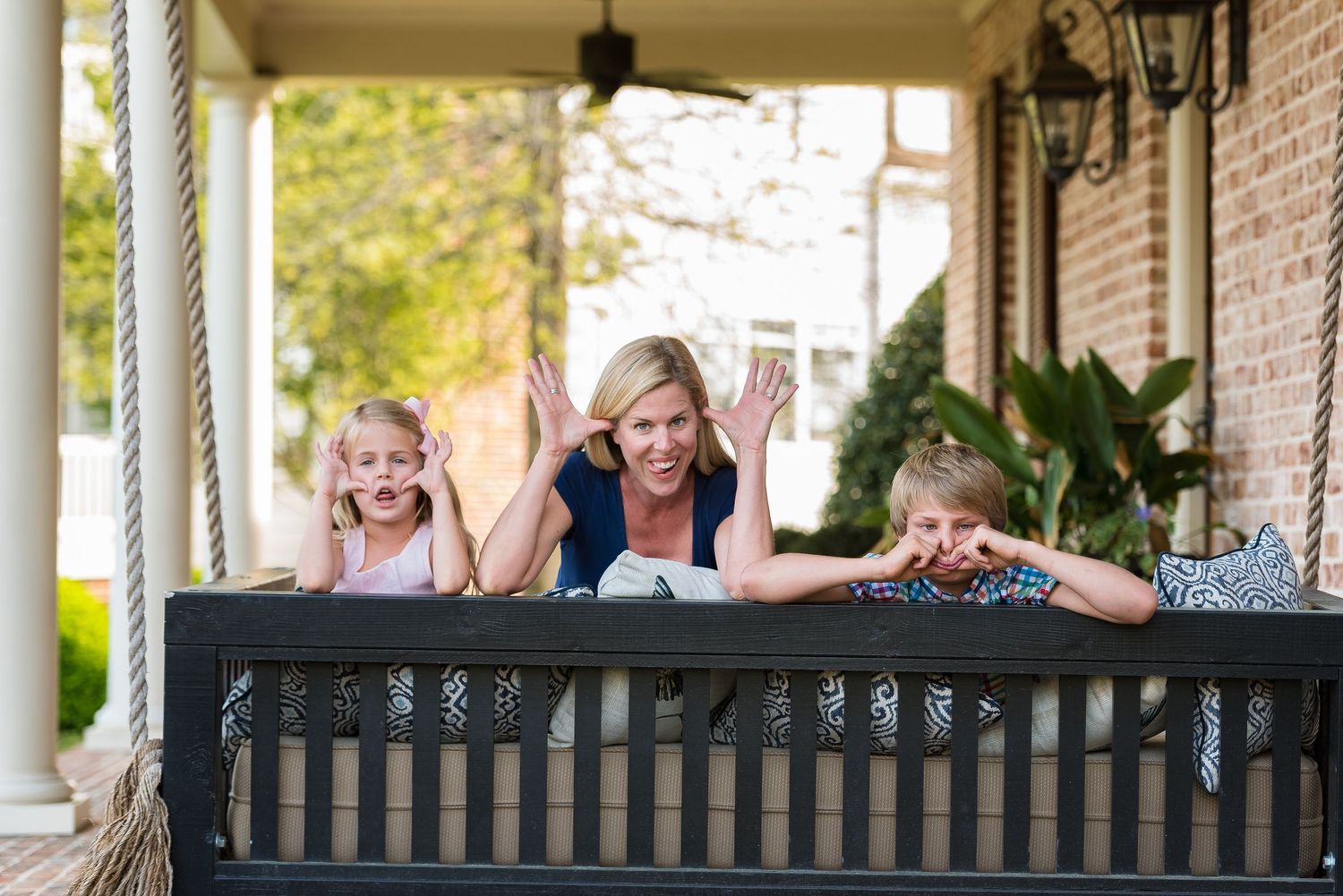 Two people lay on a porch bench making silly faces and expressions.