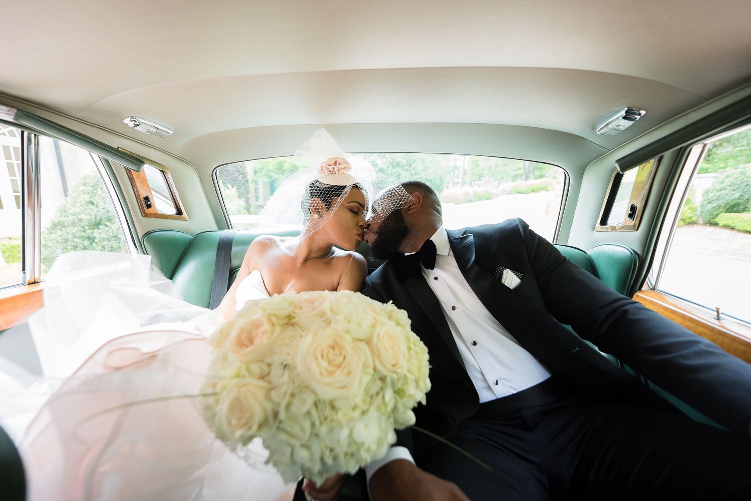 Newlyweds sharing an intimate moment in a classic car with a white bouquet.