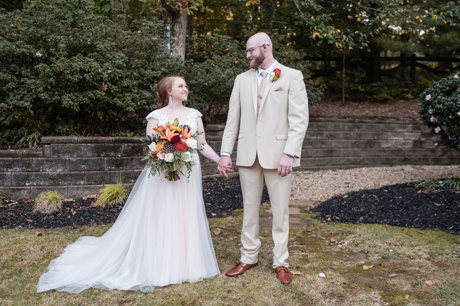 Wedding couple in white attire pose together on an autumn day with colorful floral bouquet.