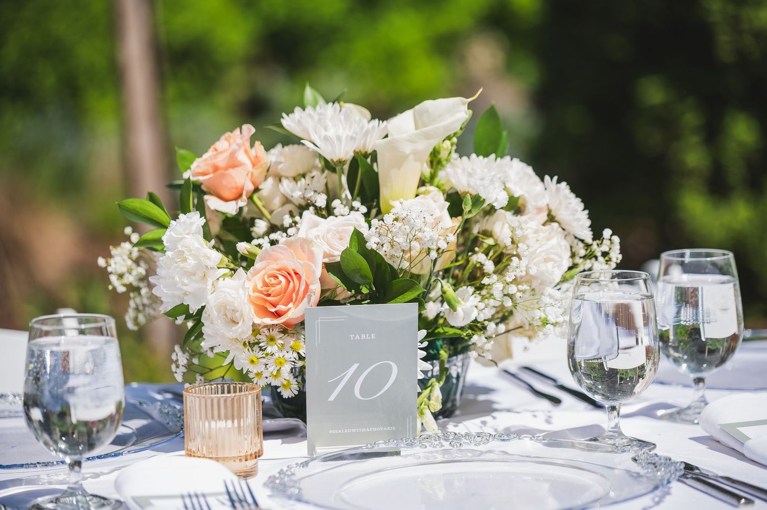 Elegant wedding table setting with peach and white floral centerpieces and glassware.