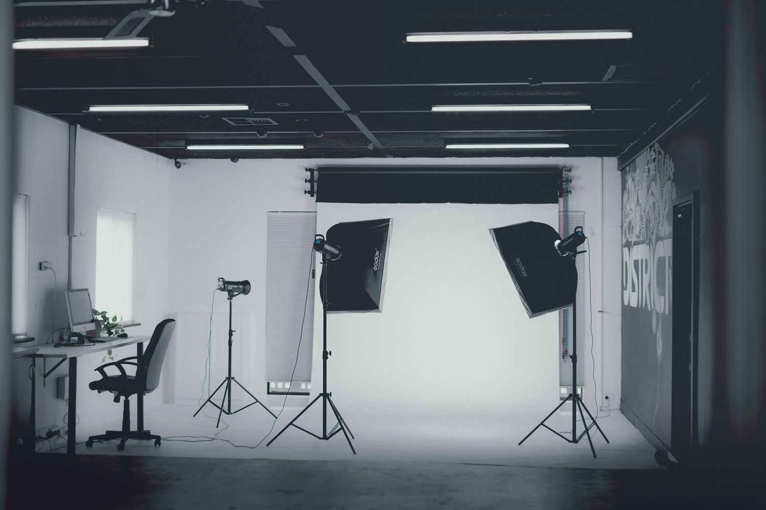 Empty photo studio interior with lighting equipment and white backdrop.