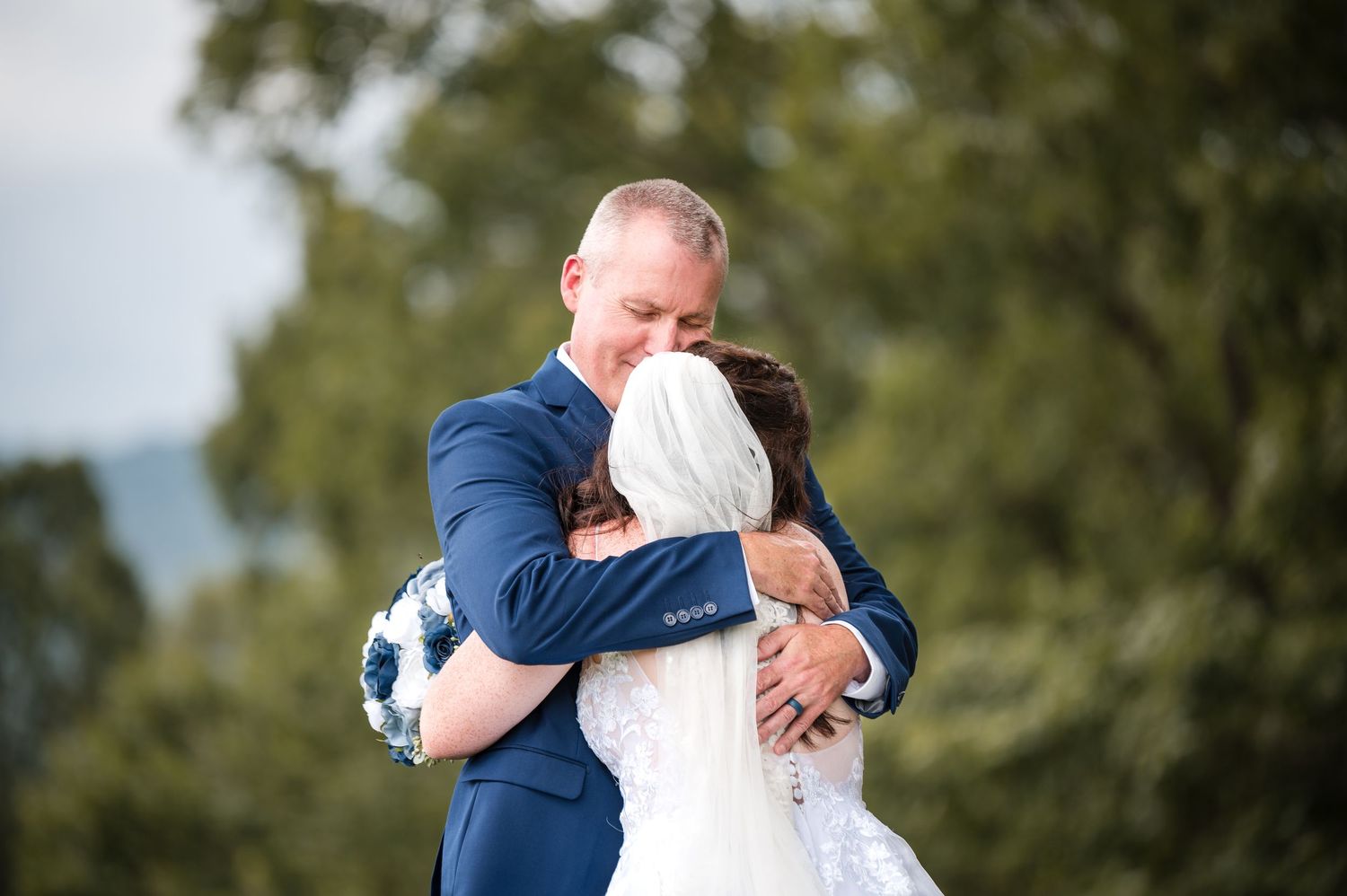 An emotional embrace between two people in formal attire during an outdoor celebration.