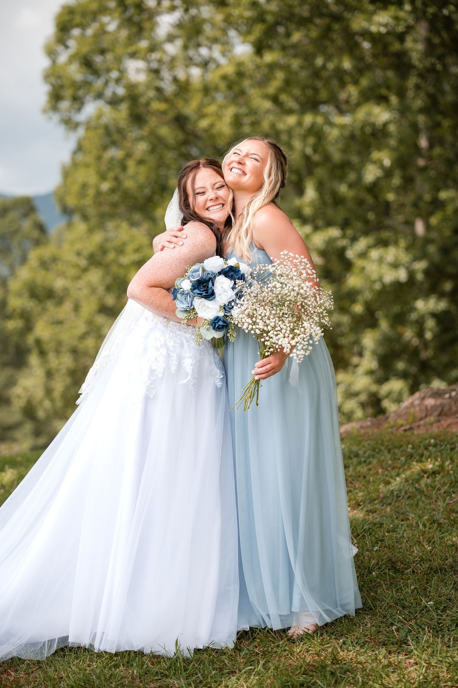 Two people in formal attire share a joyful embrace outdoors while holding a blue and white floral bouquet.