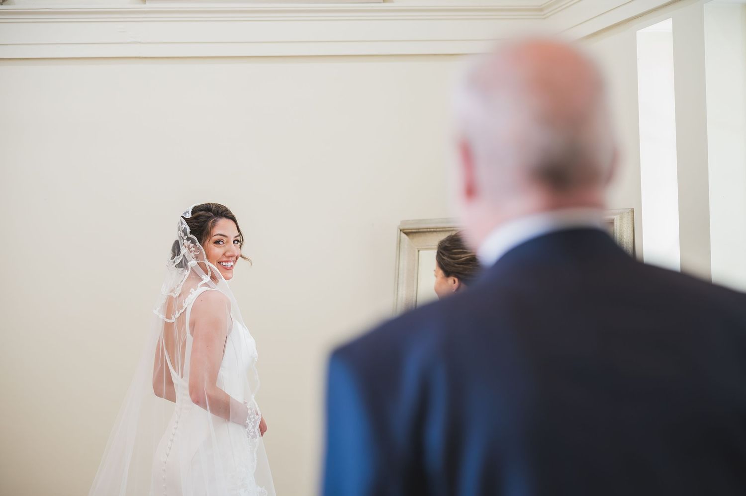 A bride in white dress looks over shoulder in bright indoor setting.