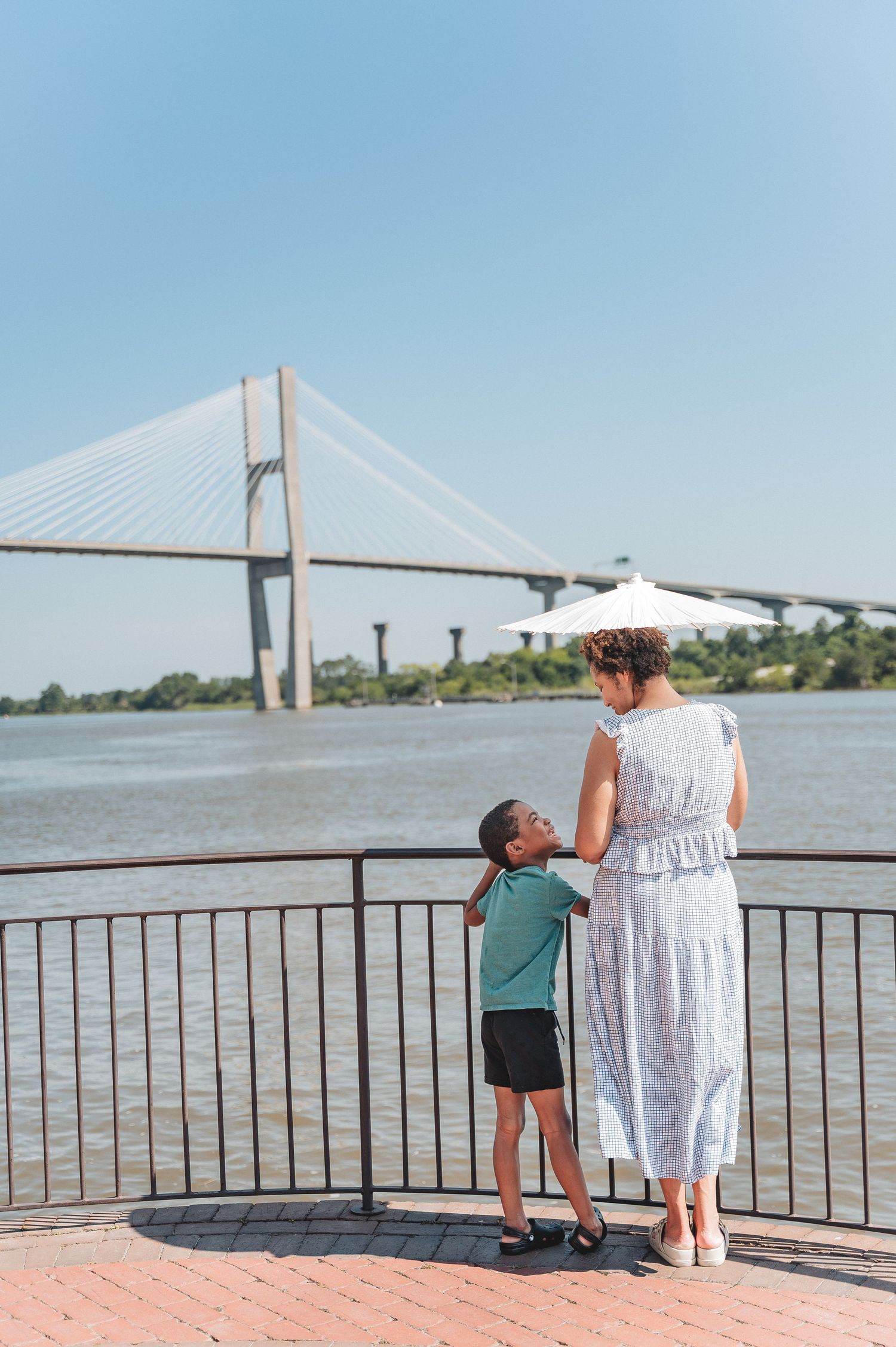 A parent and child look out over a river with a large suspension bridge in the background.