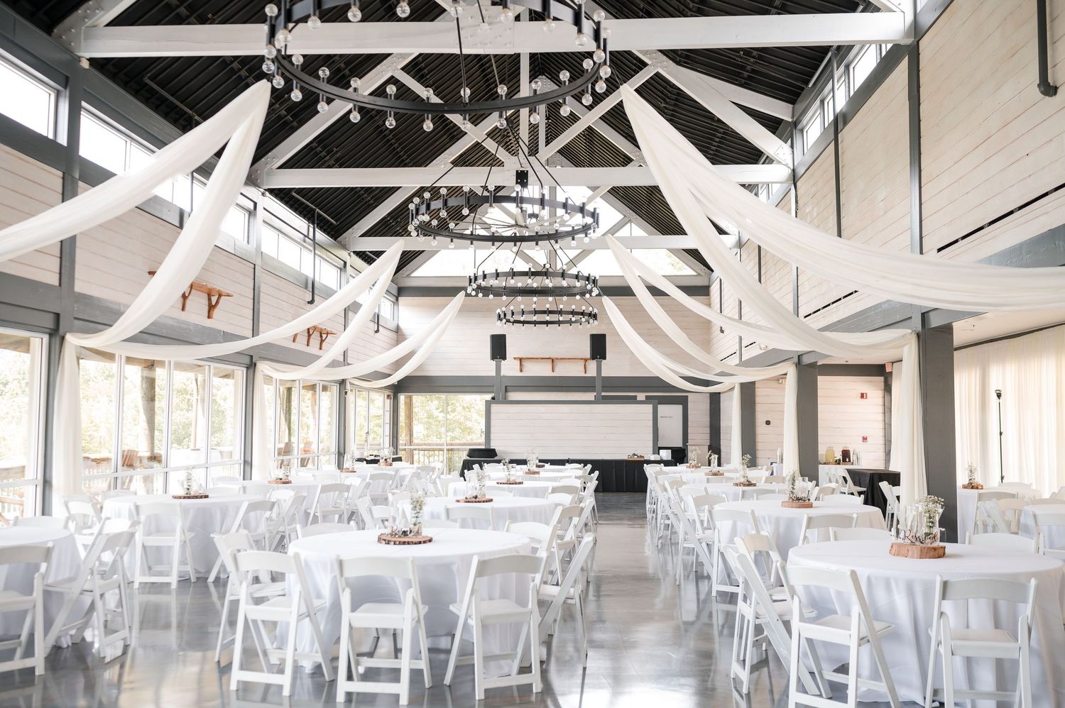 An elegant white wedding reception venue with exposed beams and hanging string lights.