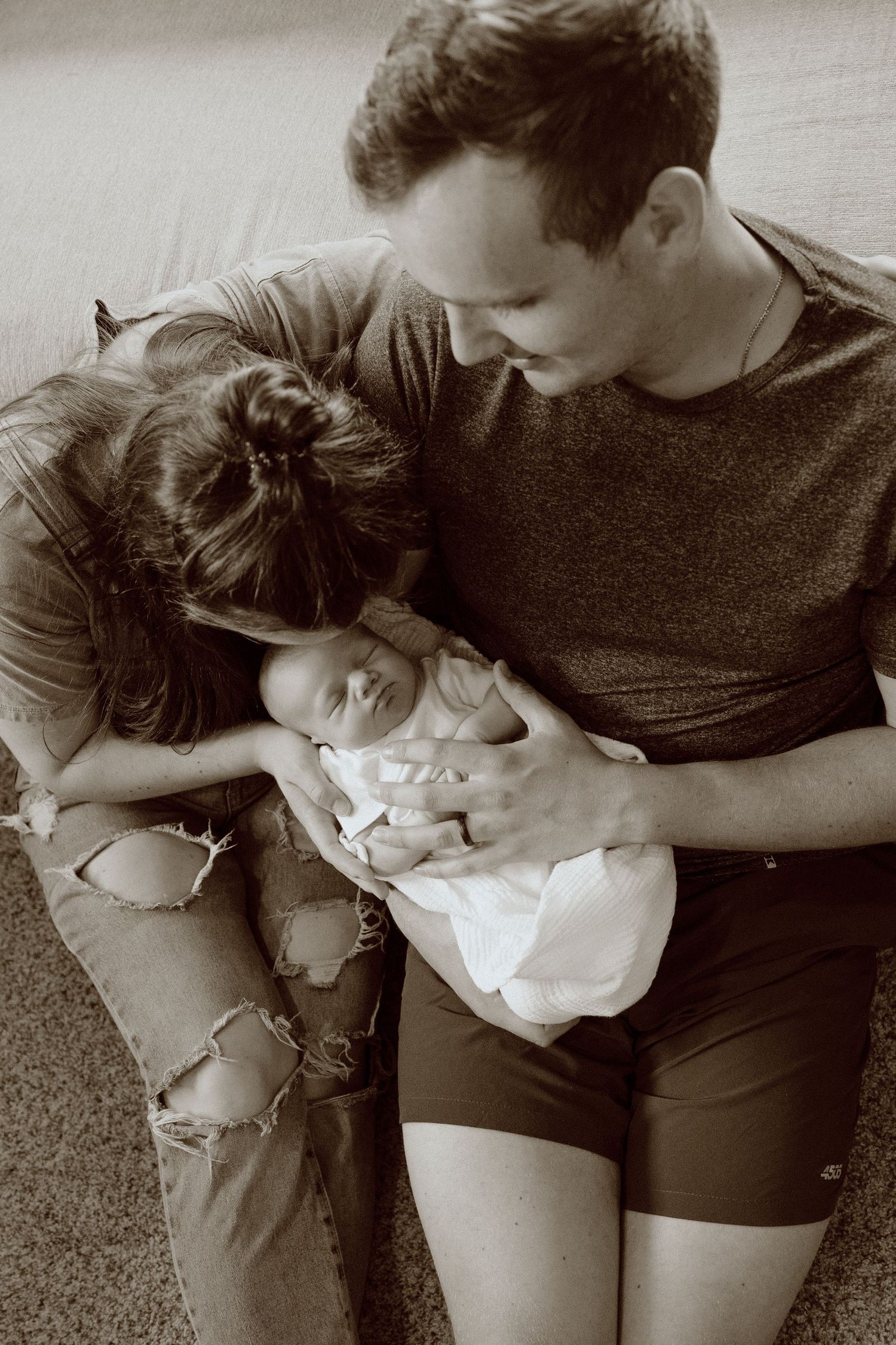 A tender black and white photo showing a couple holding and gently interacting with their sleeping baby.