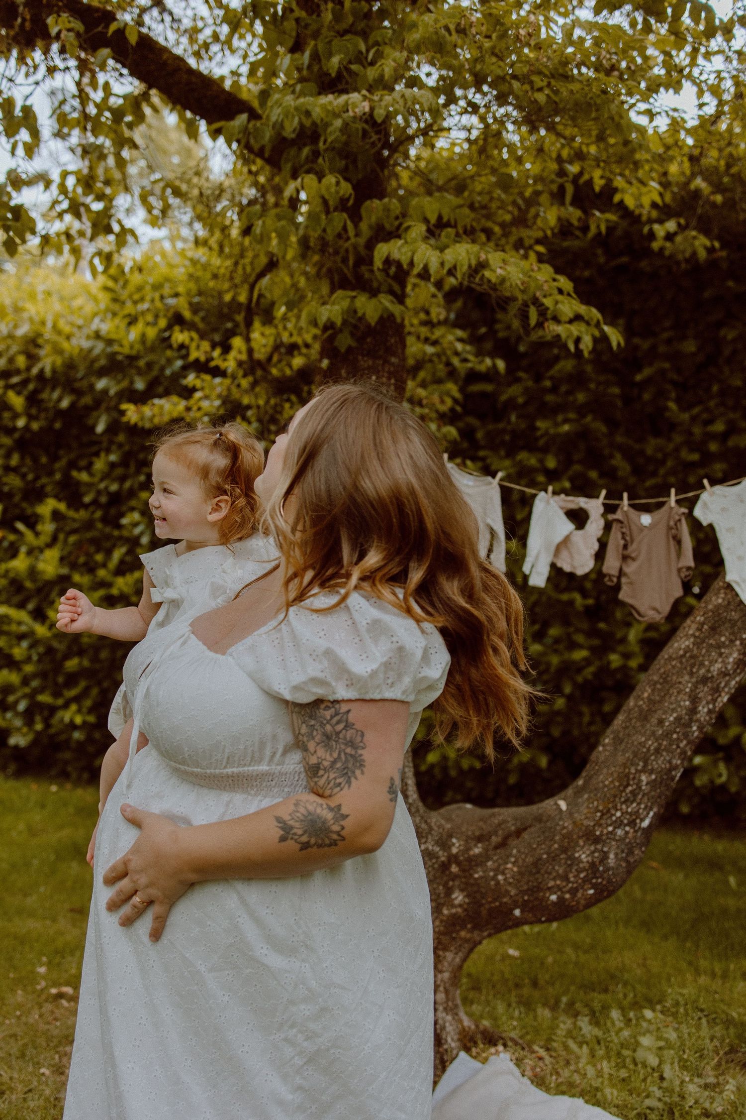 Four panels of hanging baby clothing showing a sweet hug between a parent and child in a sunlit garden setting.