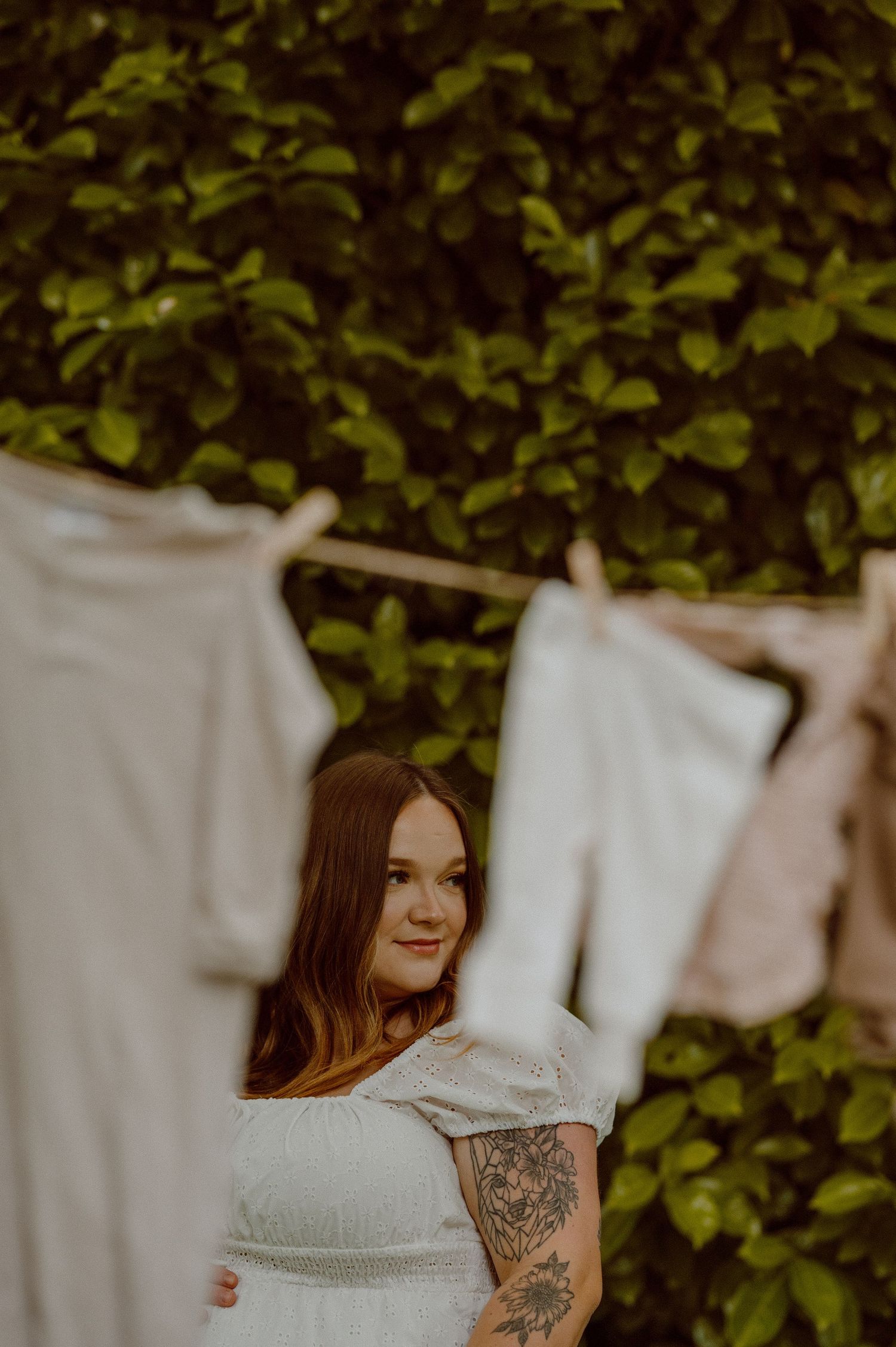 A series of blurred white fabric panels hanging outdoors against green foliage creates a dreamy backdrop.