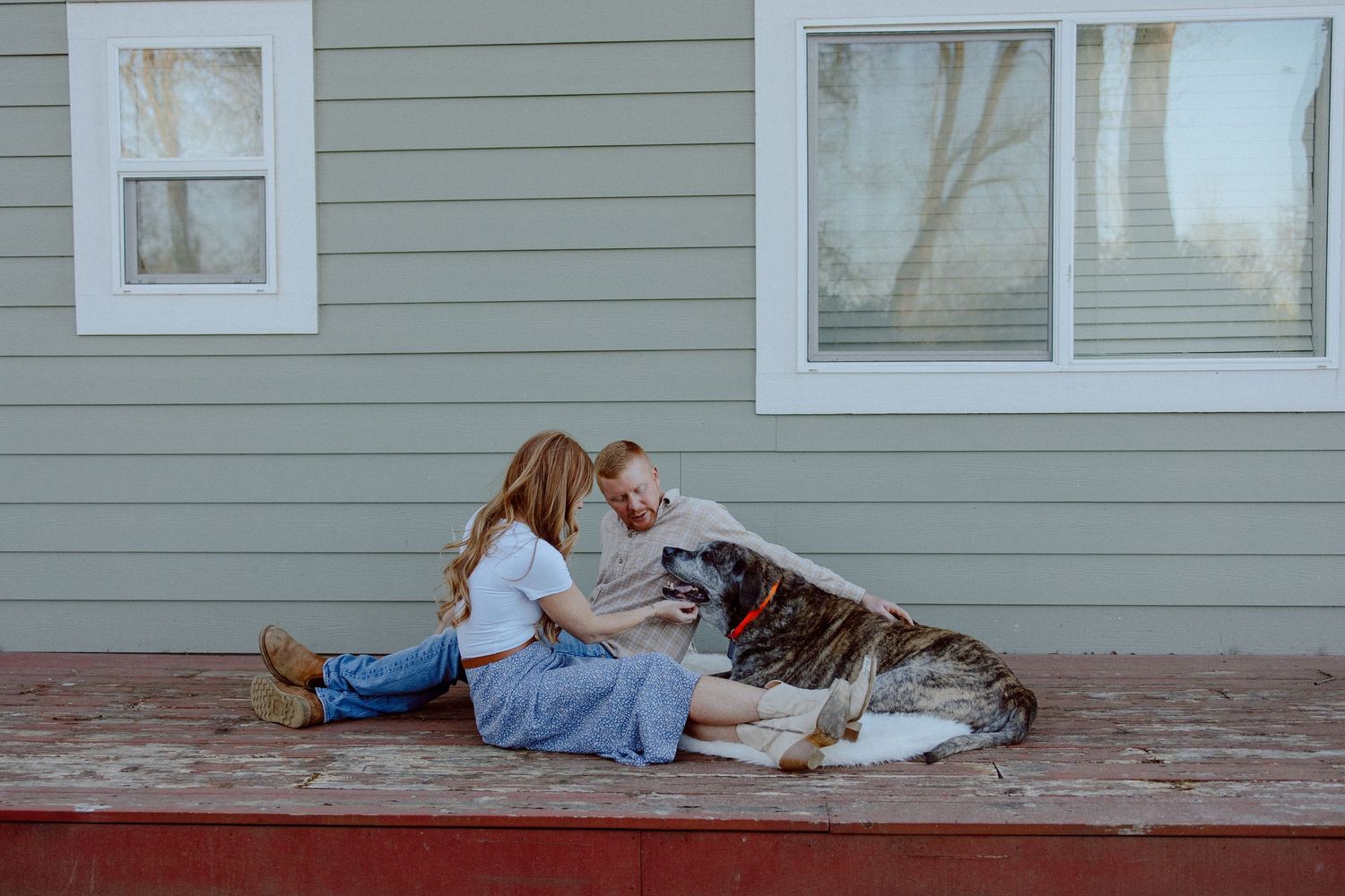An elderly dog rests alongside it's owners on a weathered wooden porch.