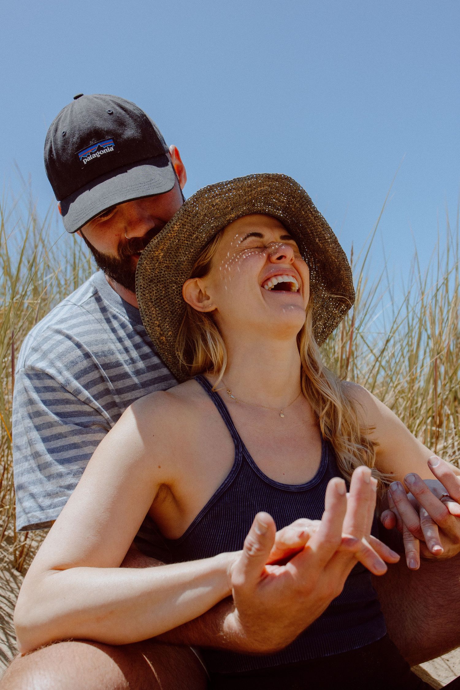 A couple shares a joyful moment together among tall grass on a sunny day at the beach.