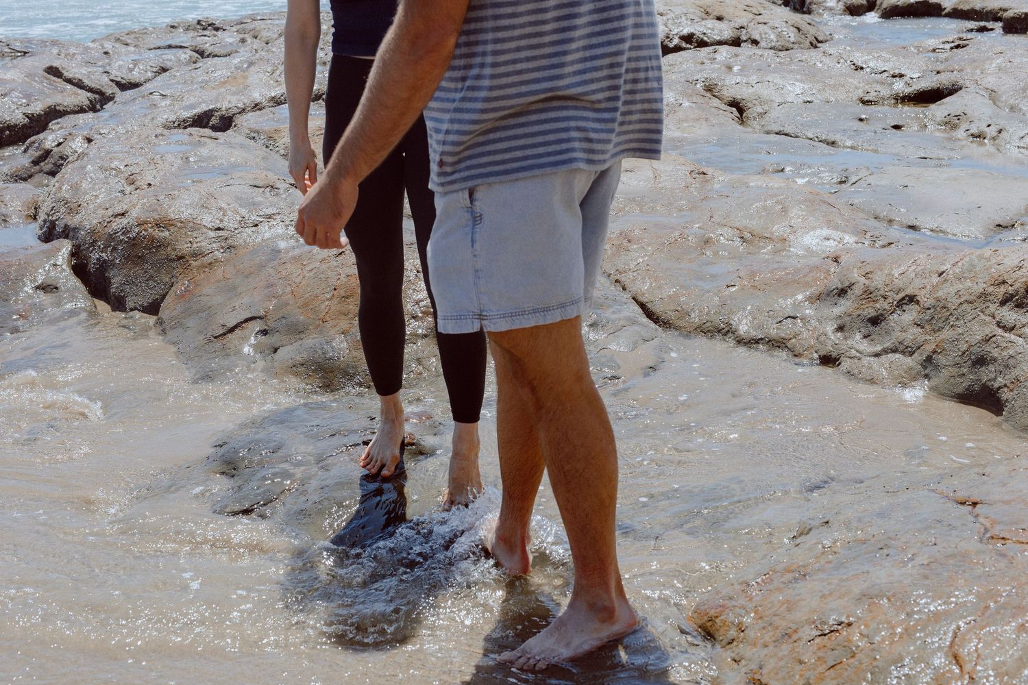 People walking through shallow water pools and jagged rock formations at the Oregon coast.