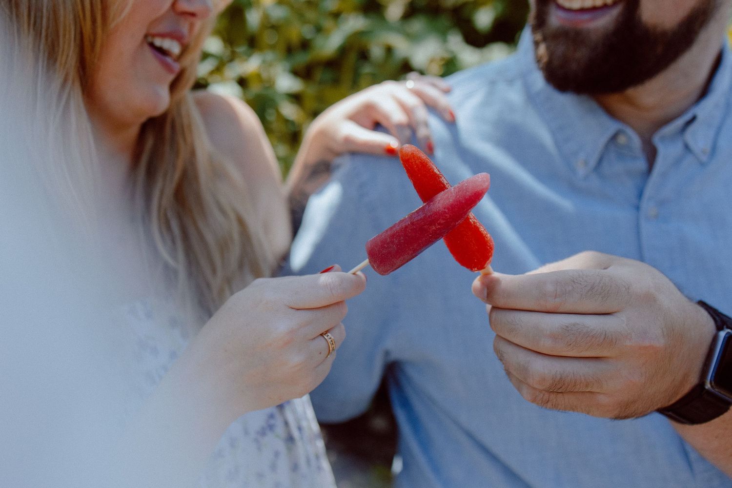 Two people sit on a stone wall sharing a romantic moment with popsicles.