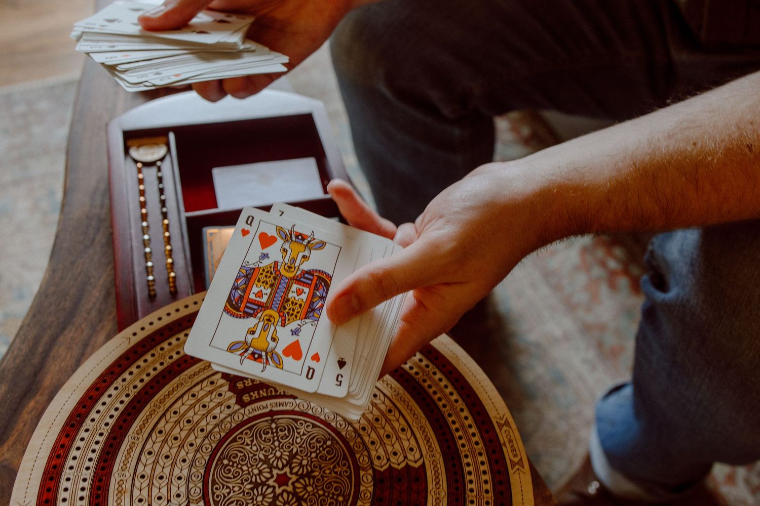 Close-up shot of hands holding cards for a game on an intricate wooden table in their living room.