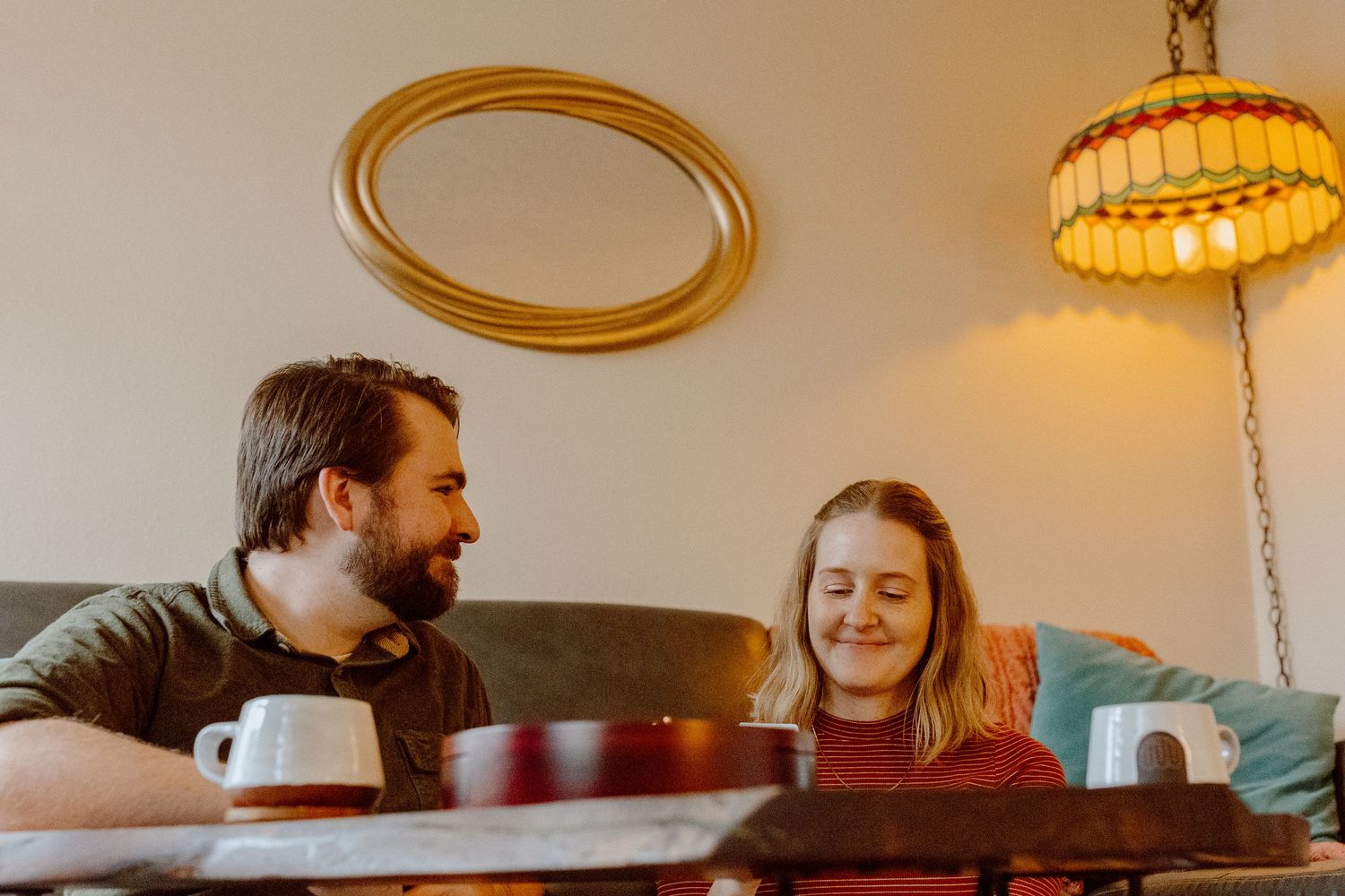Couple laughing together while sitting on the floor in a warmly lit living room setting.