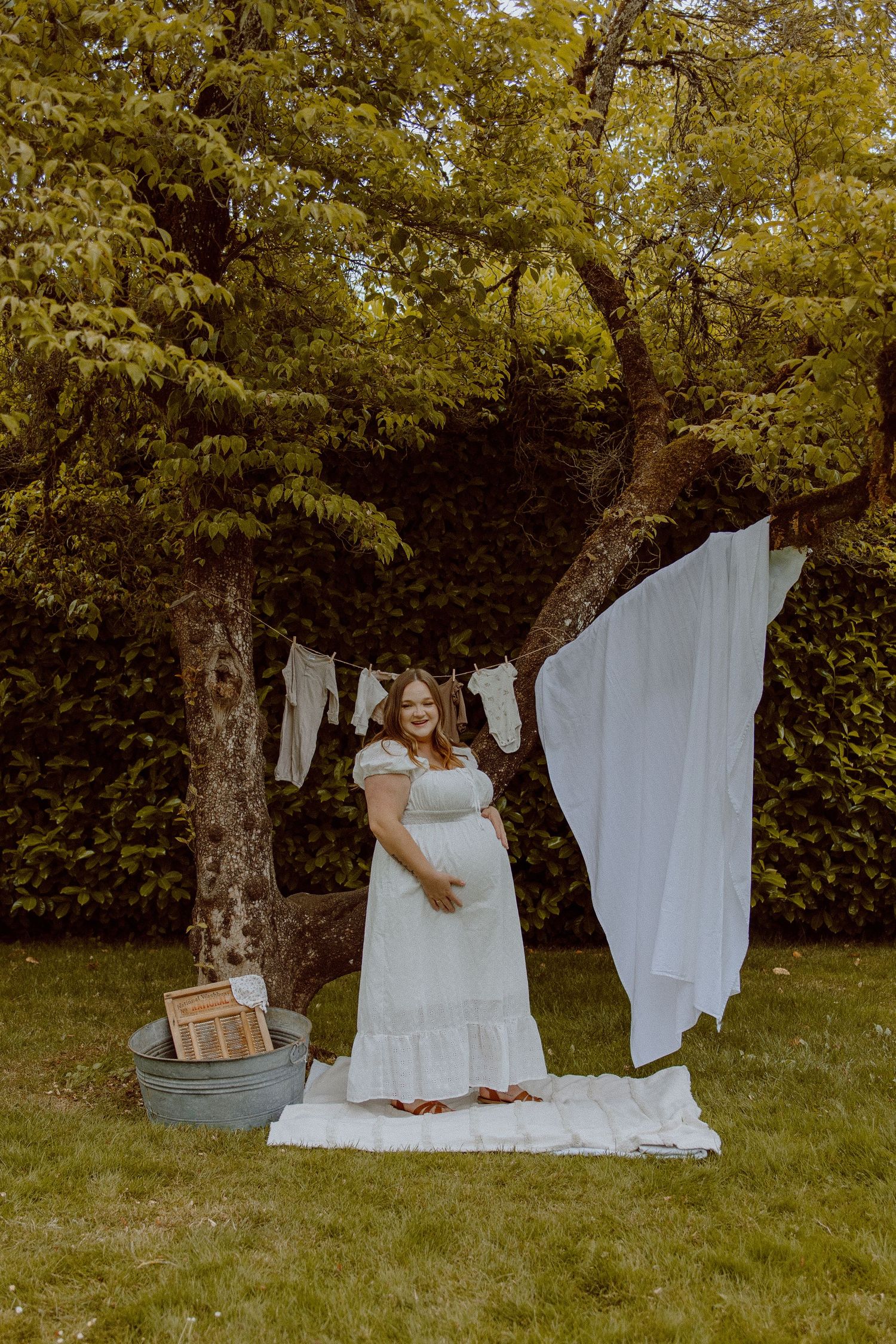 White linens hanging between trees in a lush green backyard create a dreamy outdoor laundry scene.