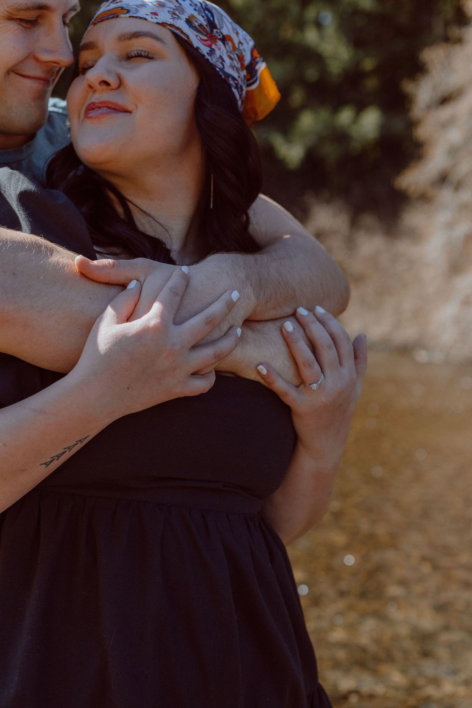 Person wearing black dress and silk head scarf showing off wedding ring outdoors in romantic photo series.