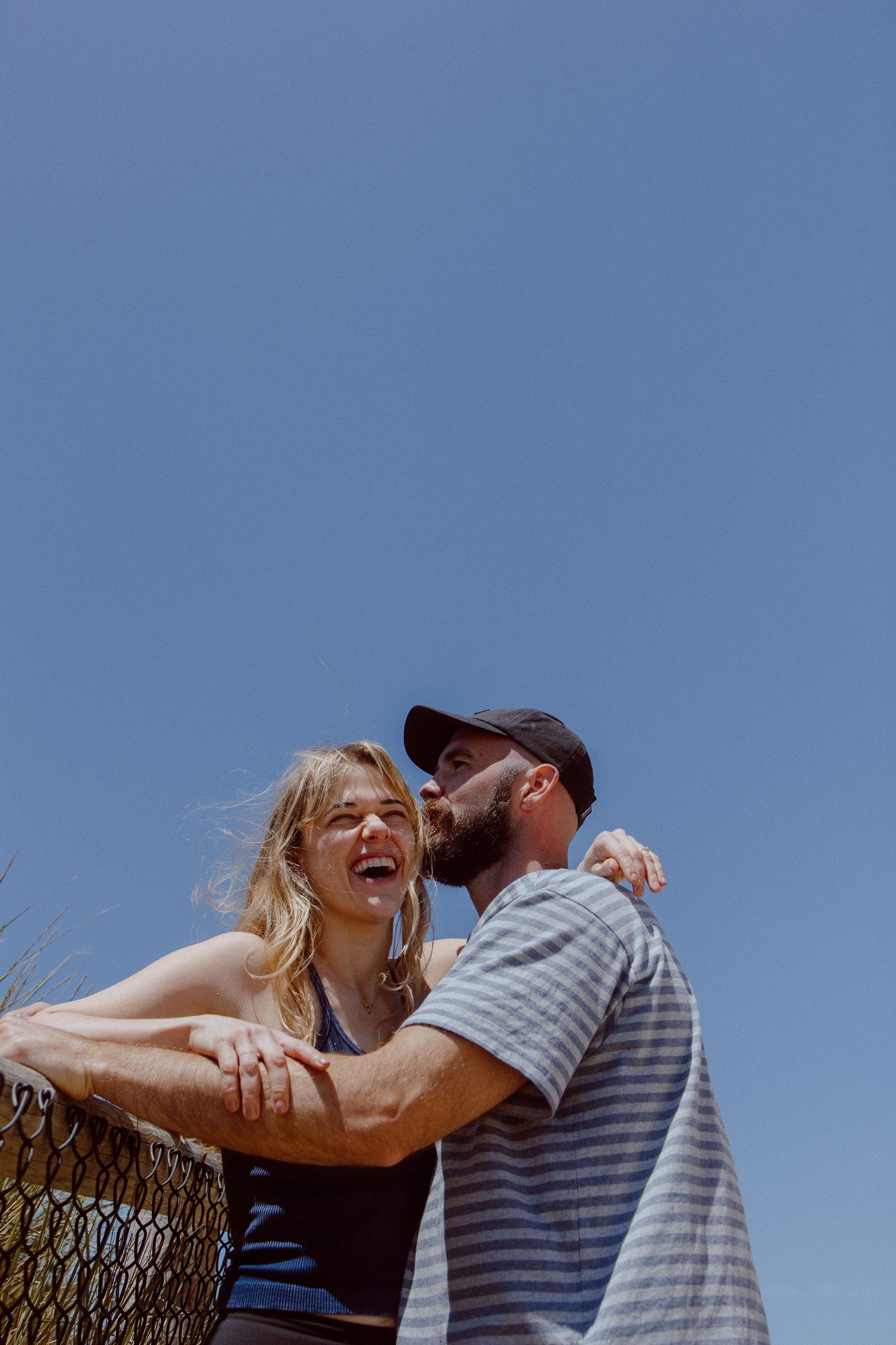 A couple sharing a joyful laugh together against a bright blue sky on a sunny day.