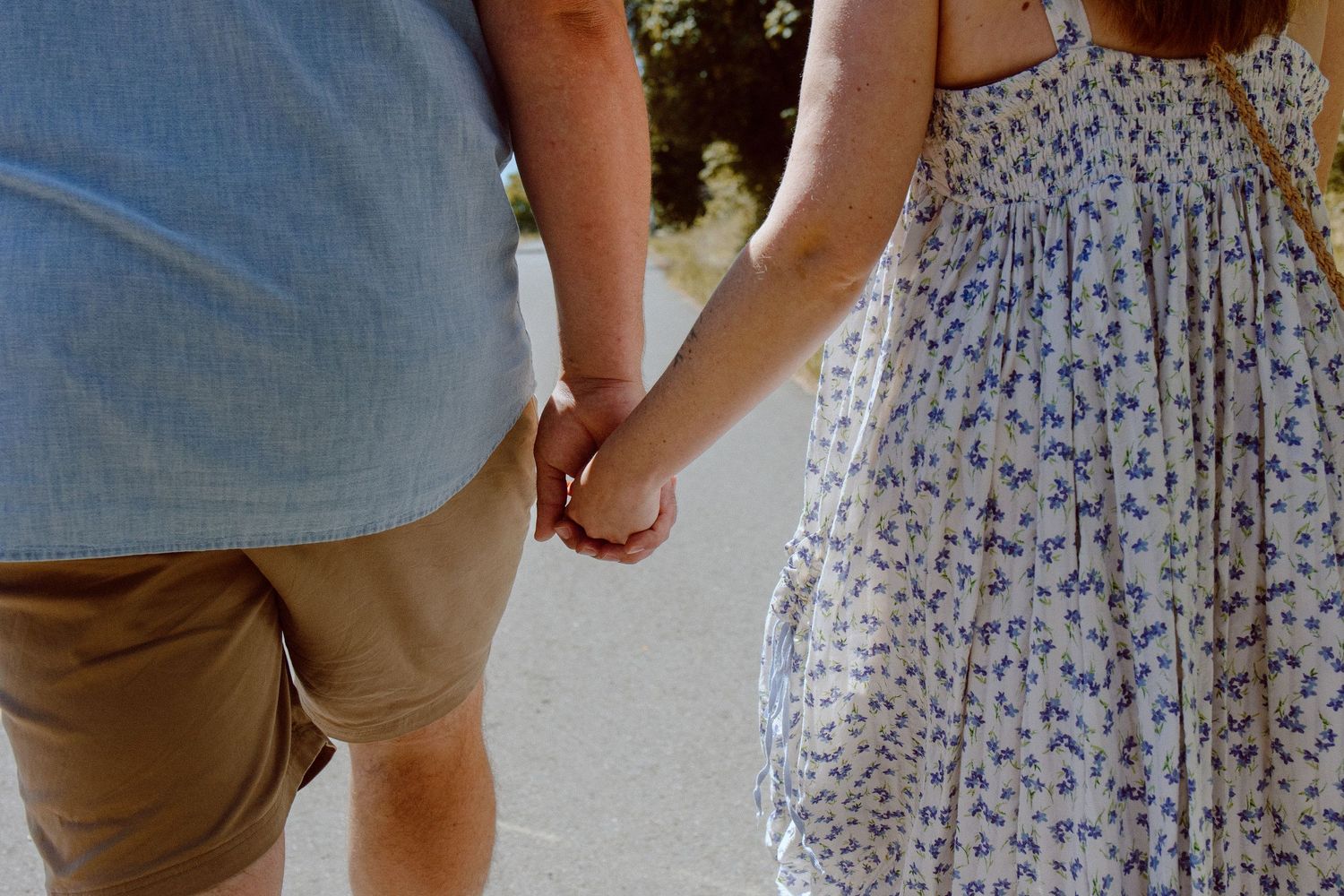 Close-up view of a couple holding hands, with person wearing tan shorts and another in a floral print dress.