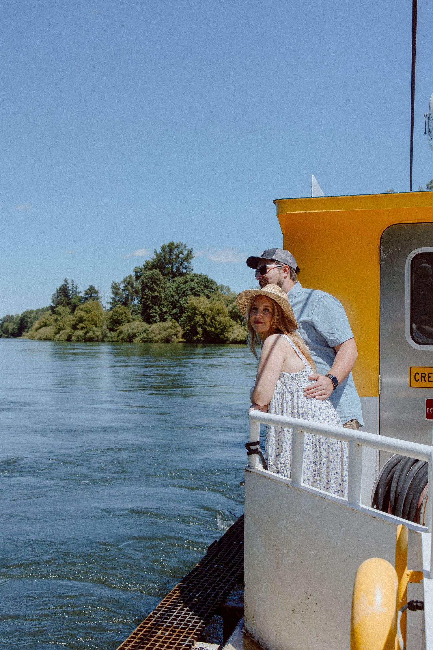 Two people enjoying a scenic boat ride on a river with blue water and green trees on a sunny day.