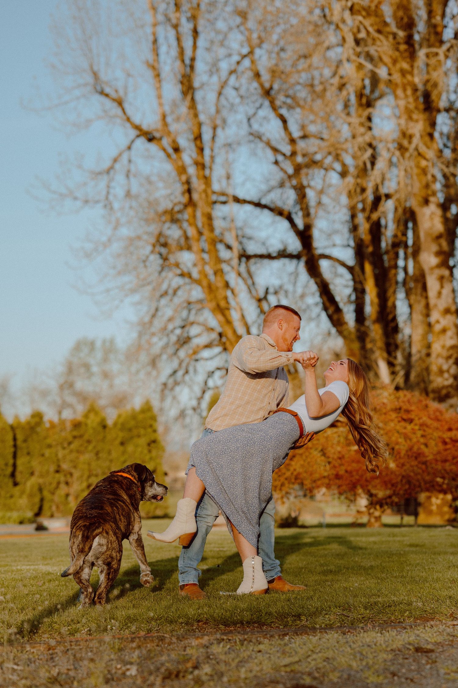 A romantic couple dances in their backyard during golden hour as their dog watches nearby in an early spring setting.