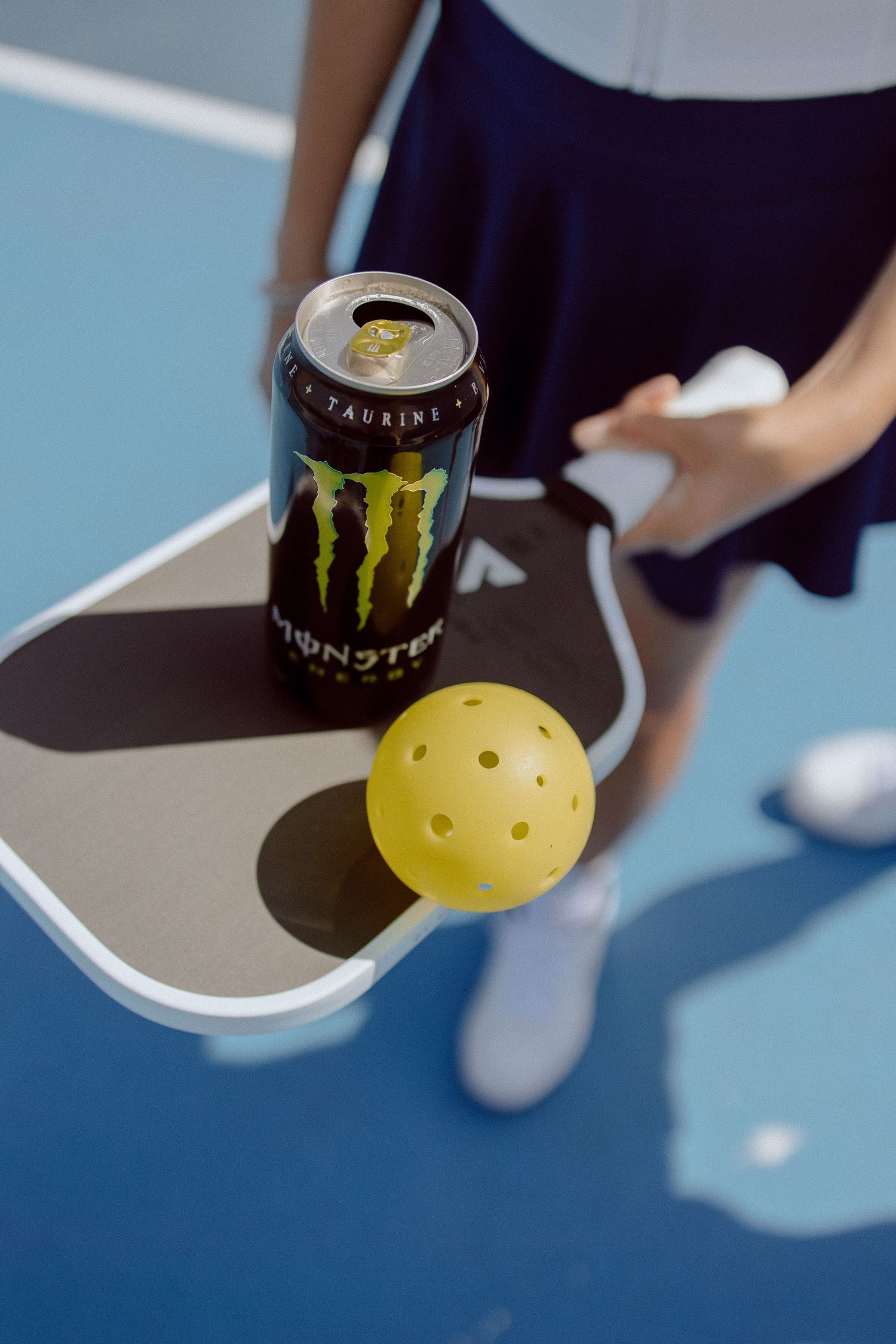 Sequence of images showing a Monster energy drink can and a pickle ball paddle being held over a blue tennis court background.
