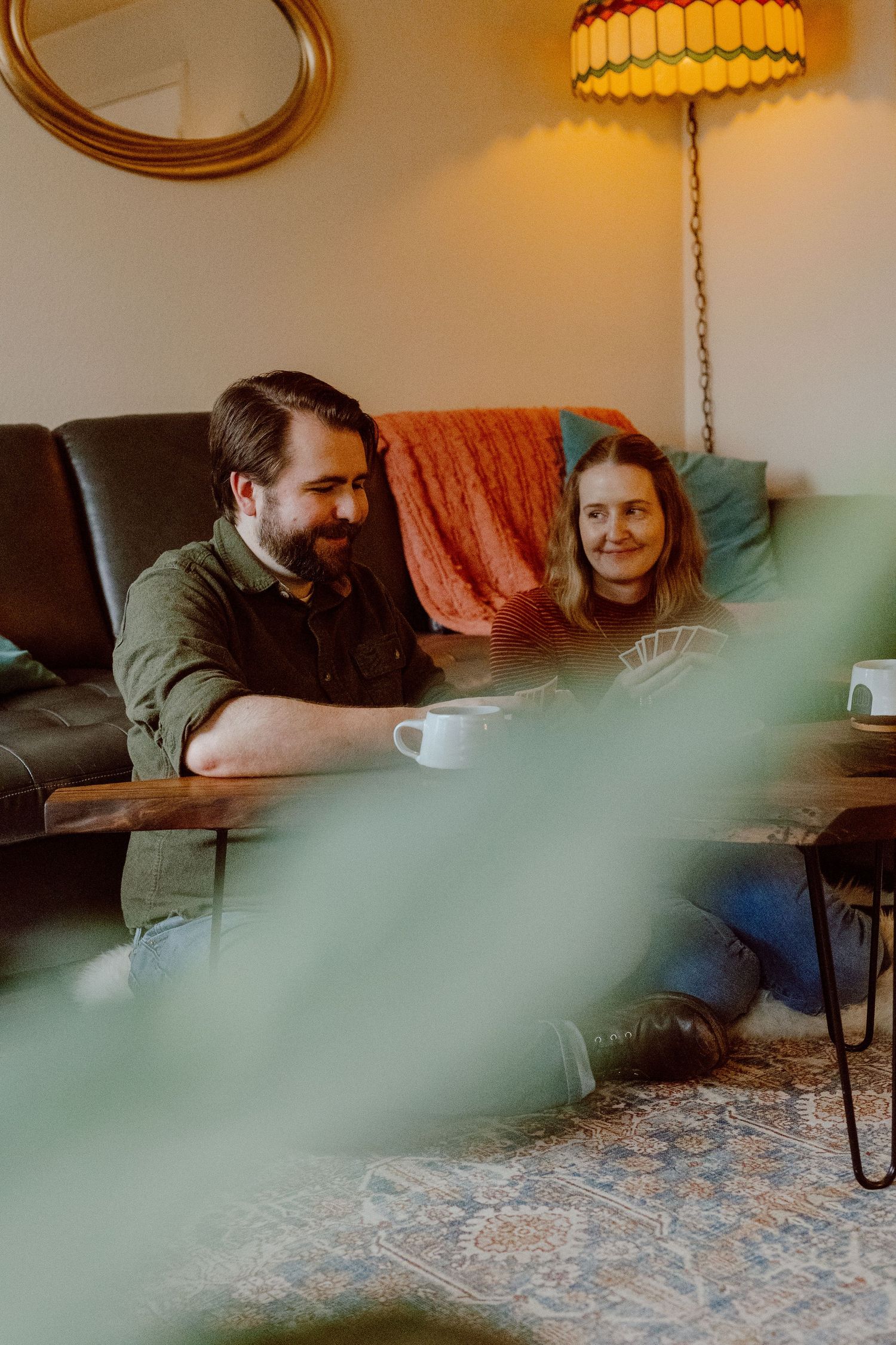 People sit together on the floor in front of their couch in a warmly lit living room with a coffee mug.